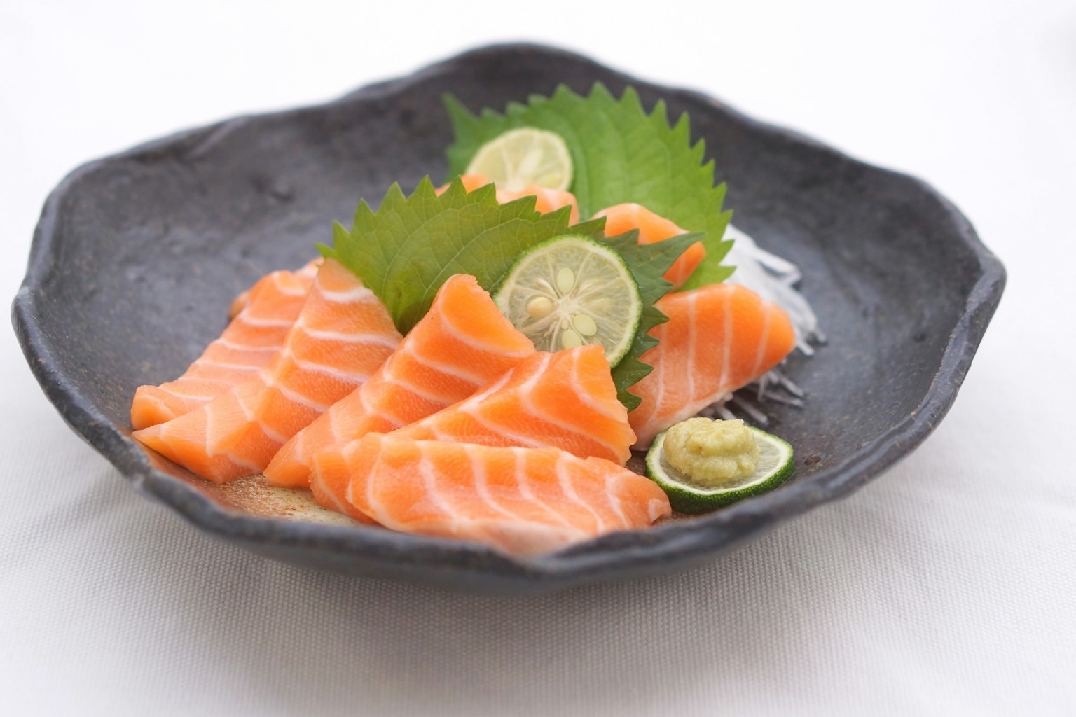 Fresh salmon sashimi arranged on a black plate with lime and wasabi