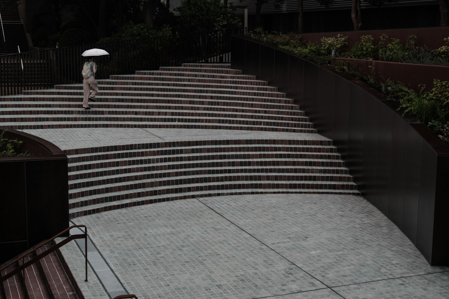 Person mit einem Regenschirm, der eine moderne Treppe mit Pflanzen umgibt, hinaufgeht