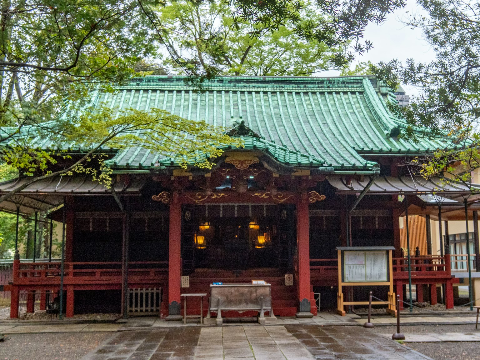 神社建筑，绿屋顶和红柱，四周被茂密的树木环绕