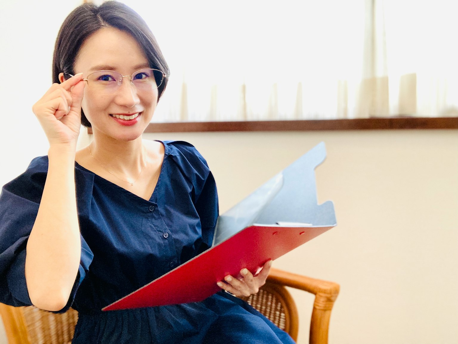 Seorang wanita mengenakan kacamata tersenyum sambil memegang folder merah