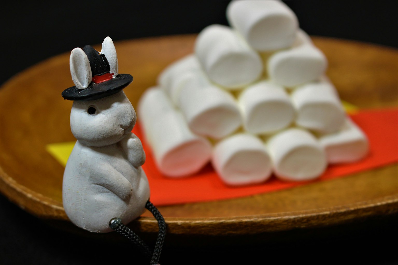 A figurine of a rabbit wearing a hat beside a pyramid of marshmallows on a wooden plate