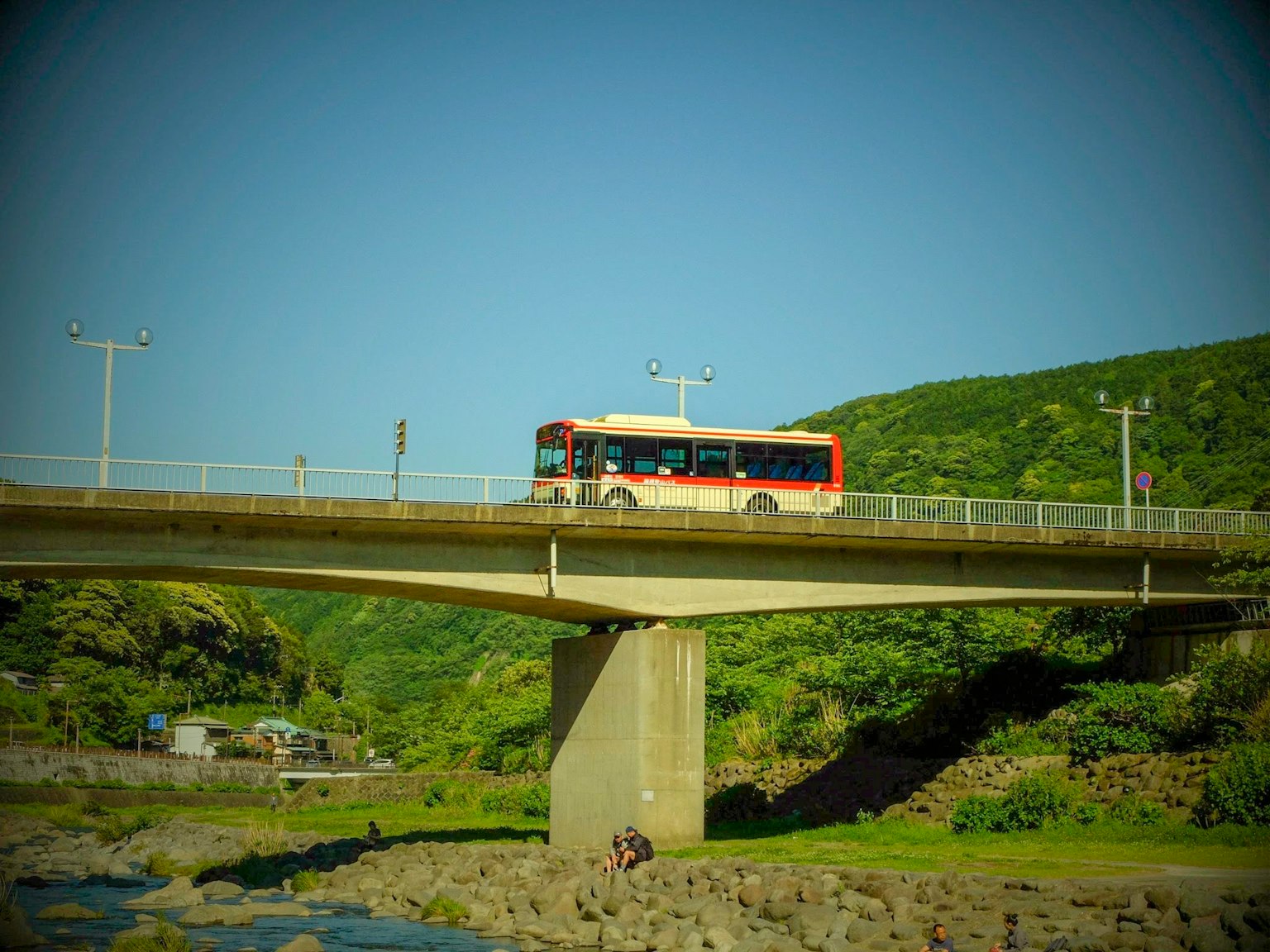 Un autobus che attraversa un ponte con montagne verdi e cielo blu sullo sfondo