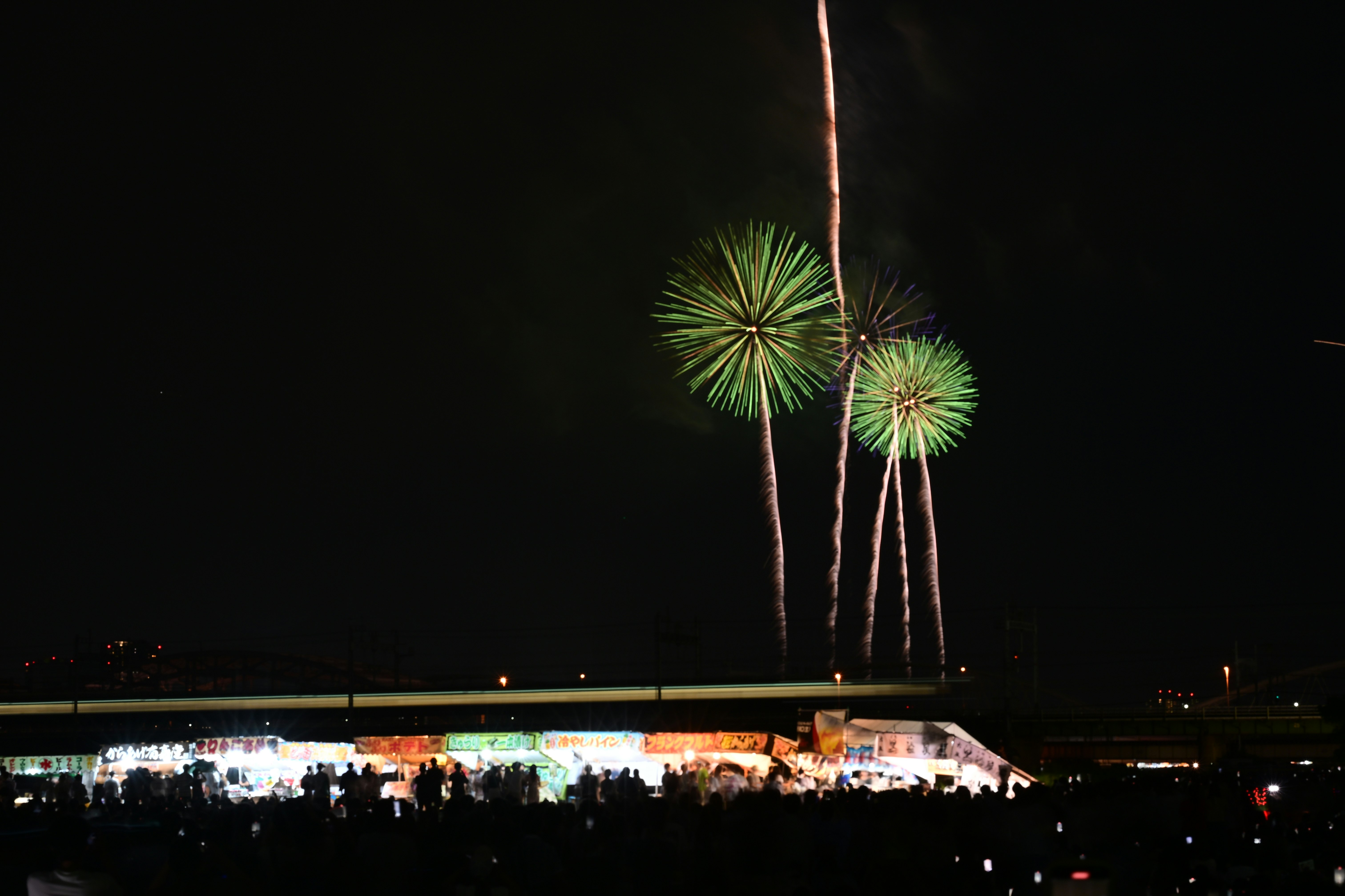 夜空に打ち上がる花火と海辺のイベント会場の灯り