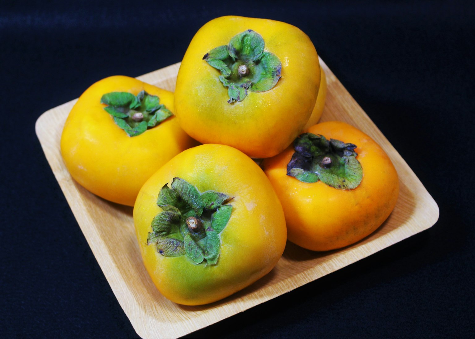 Yellow persimmons arranged on a wooden plate