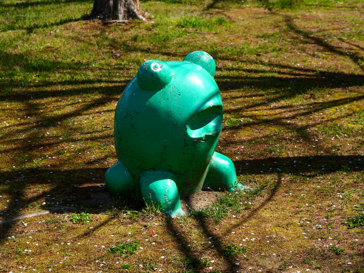 Escultura de rana verde en un parque con sombras