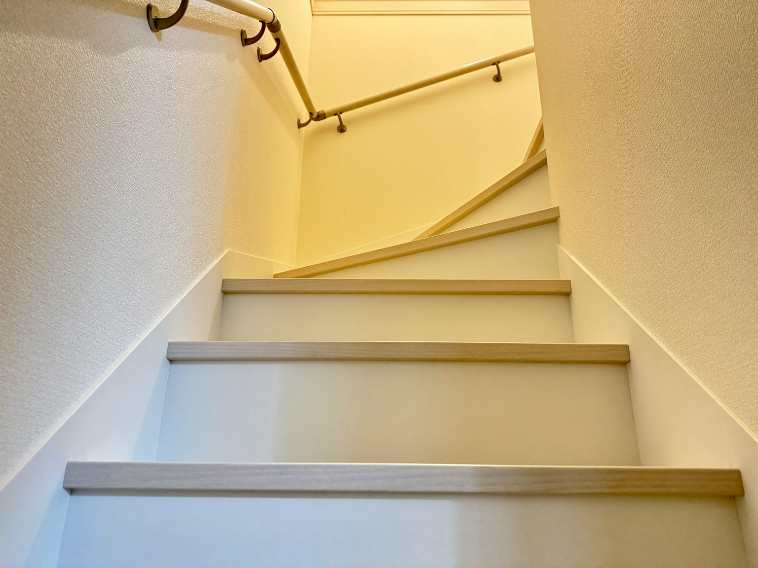 Helle Treppe mit weißen Wänden und einem Handlauf, der nach oben führt