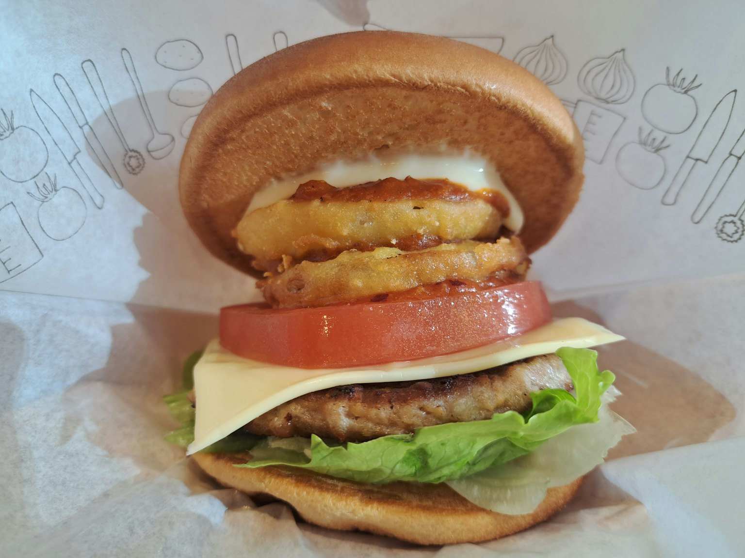 Delicious hamburger image featuring lettuce, tomato, cheese, patty, and onion rings