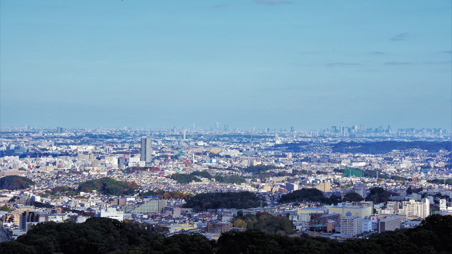 Pemandangan panorama kota di bawah langit biru dengan bukit hijau dan bangunan