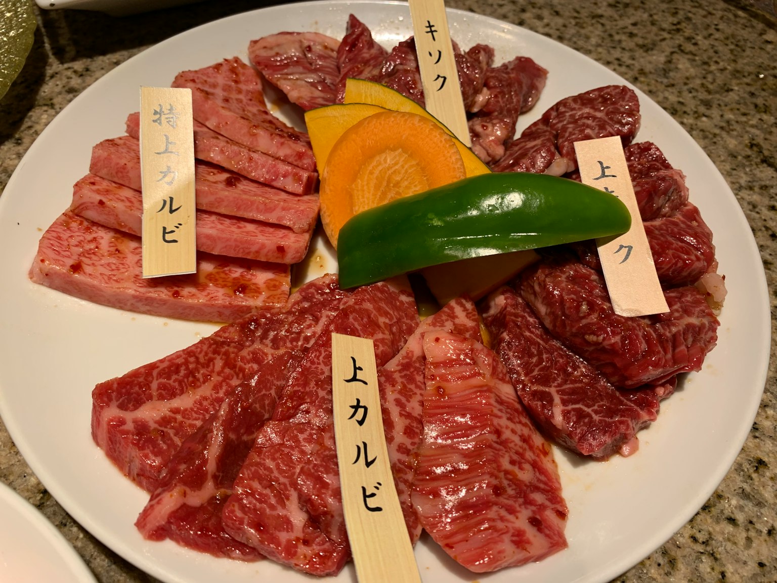 Plateau de viandes assorties avec des étiquettes et des légumes disposés sur une assiette blanche