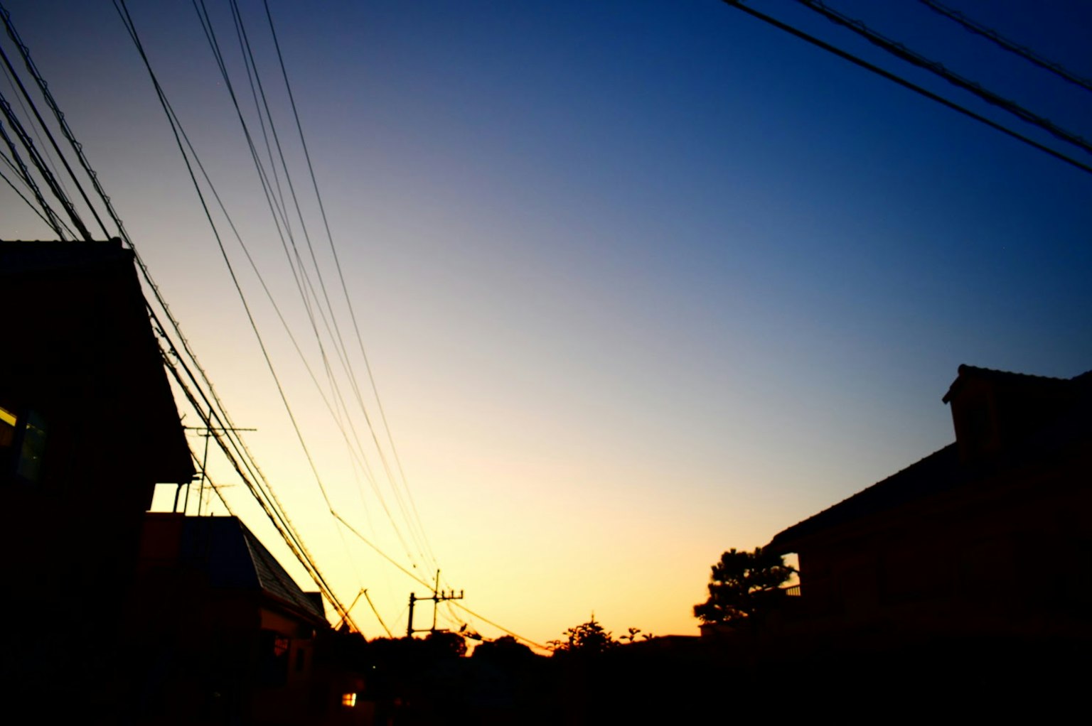 Siluet bangunan di latar belakang langit senja dengan kabel listrik