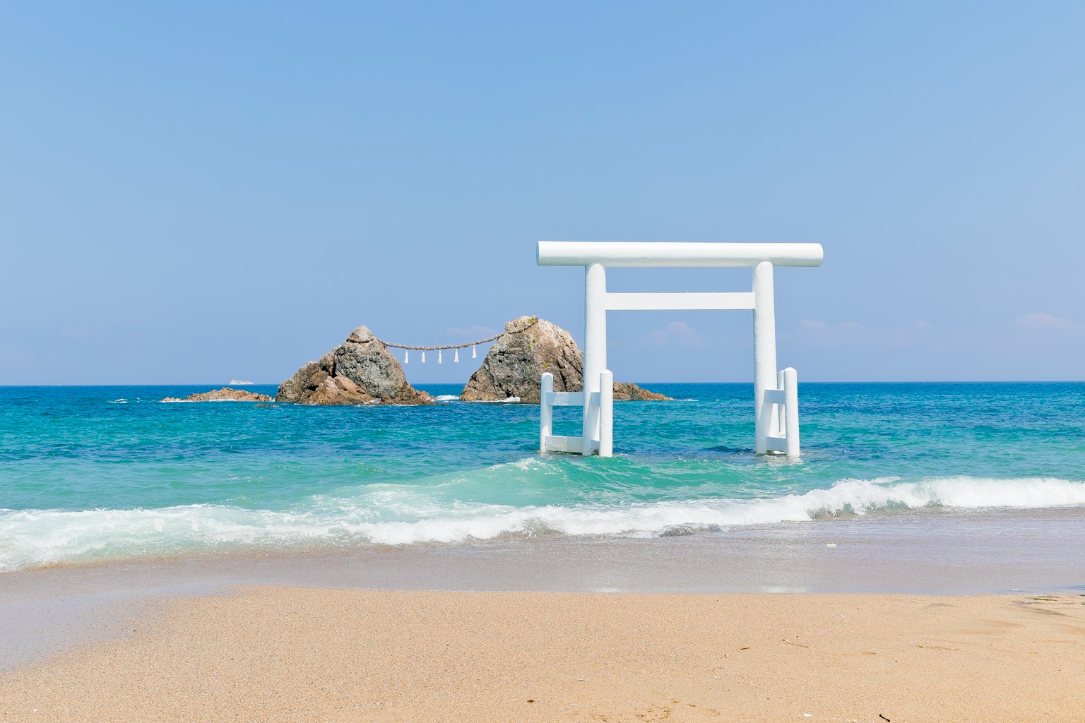Un torii blanc se dresse dans l'océan sur une belle plage
