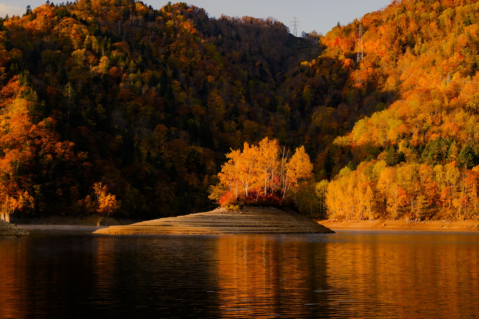 秋の色彩に包まれた山々と静かな湖の風景 小さな島に立つ木々が美しい反射を見せる