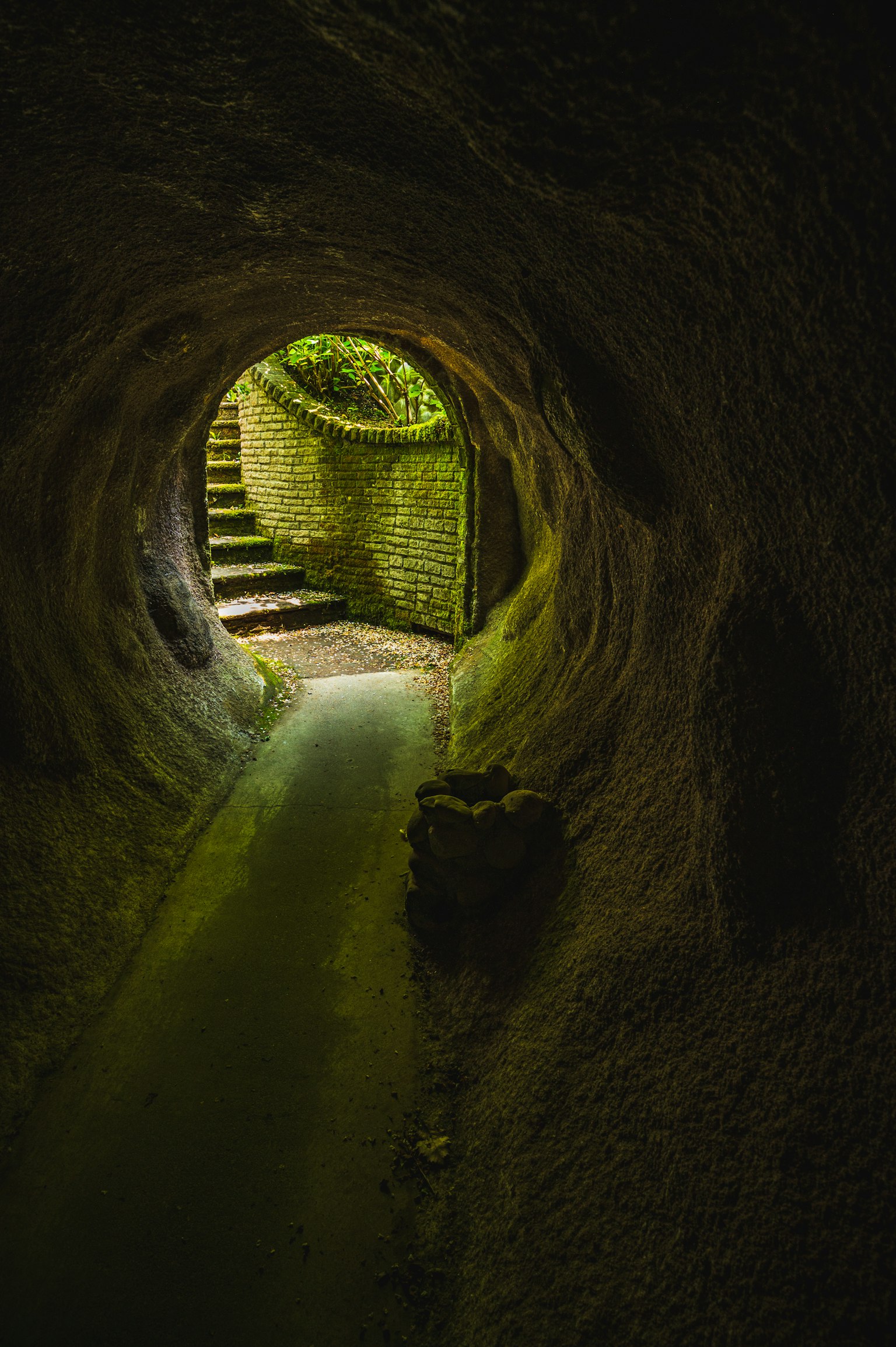 A tunnel with green light at the end and visible stairs