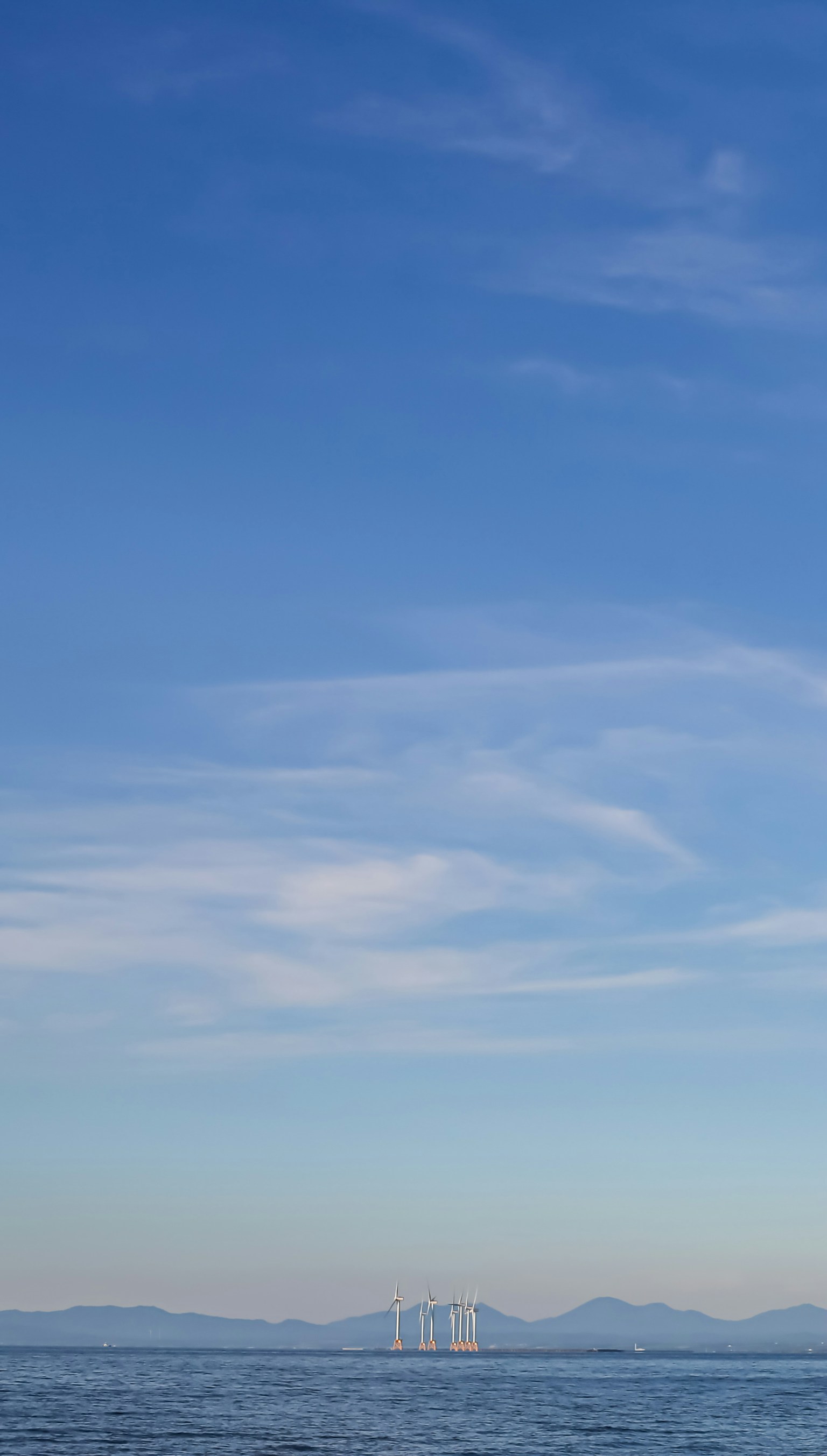 A serene landscape featuring a blue sky and calm sea with distant mountain silhouettes