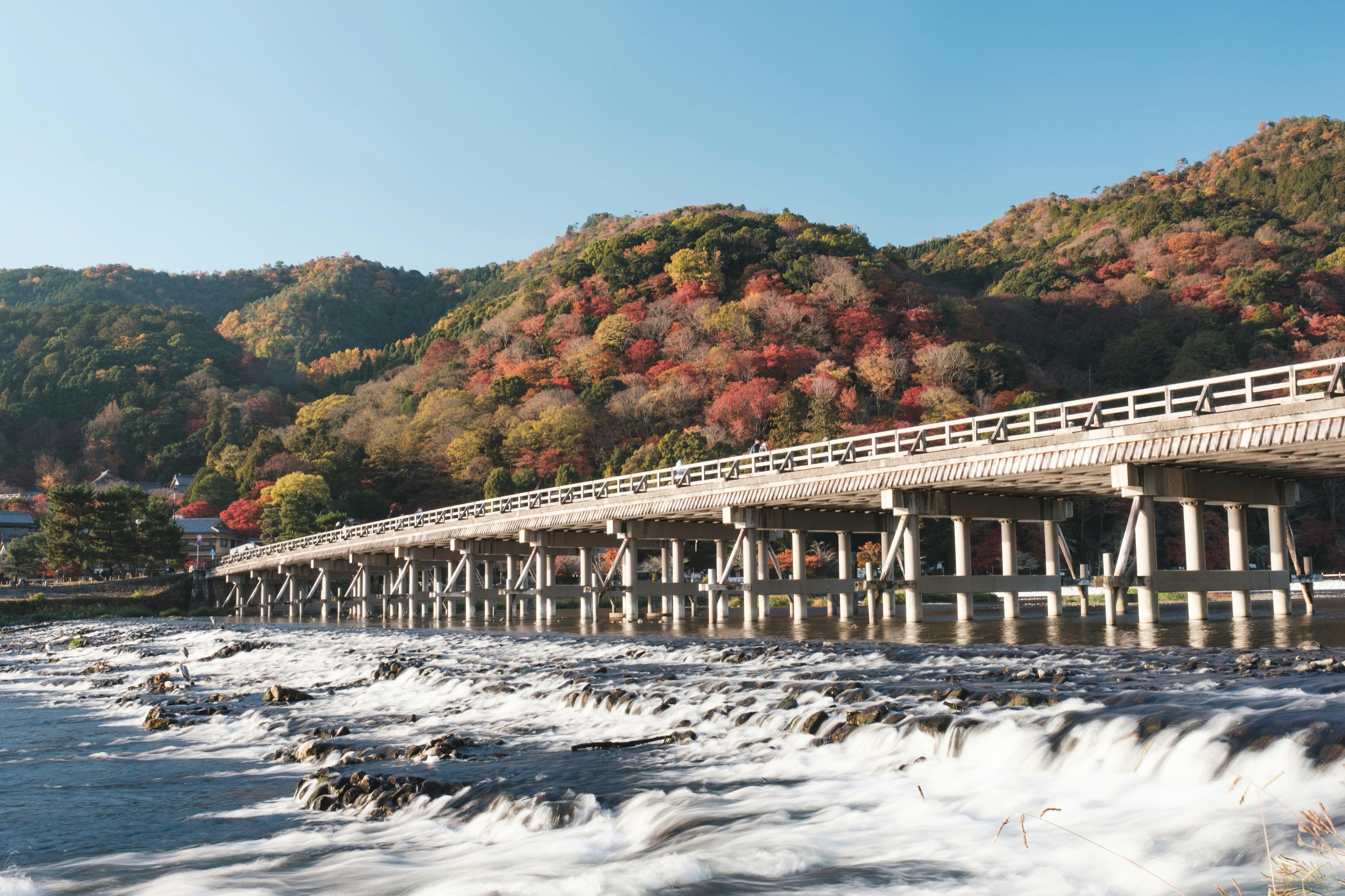 紅葉の山並みと川を渡る長い橋の風景