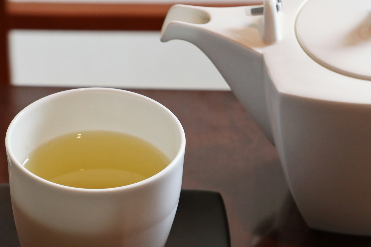 白色茶壶旁边的白色杯子里的绿茶图像