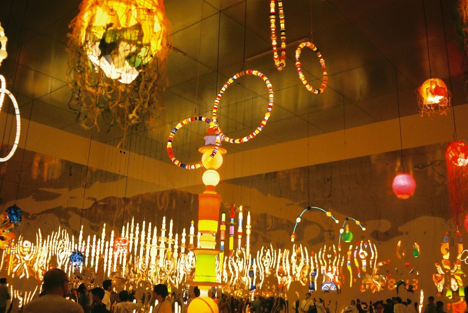 Scène intérieure avec des décorations illuminées colorées comprenant de nombreuses lampes suspendues et des objets lumineux