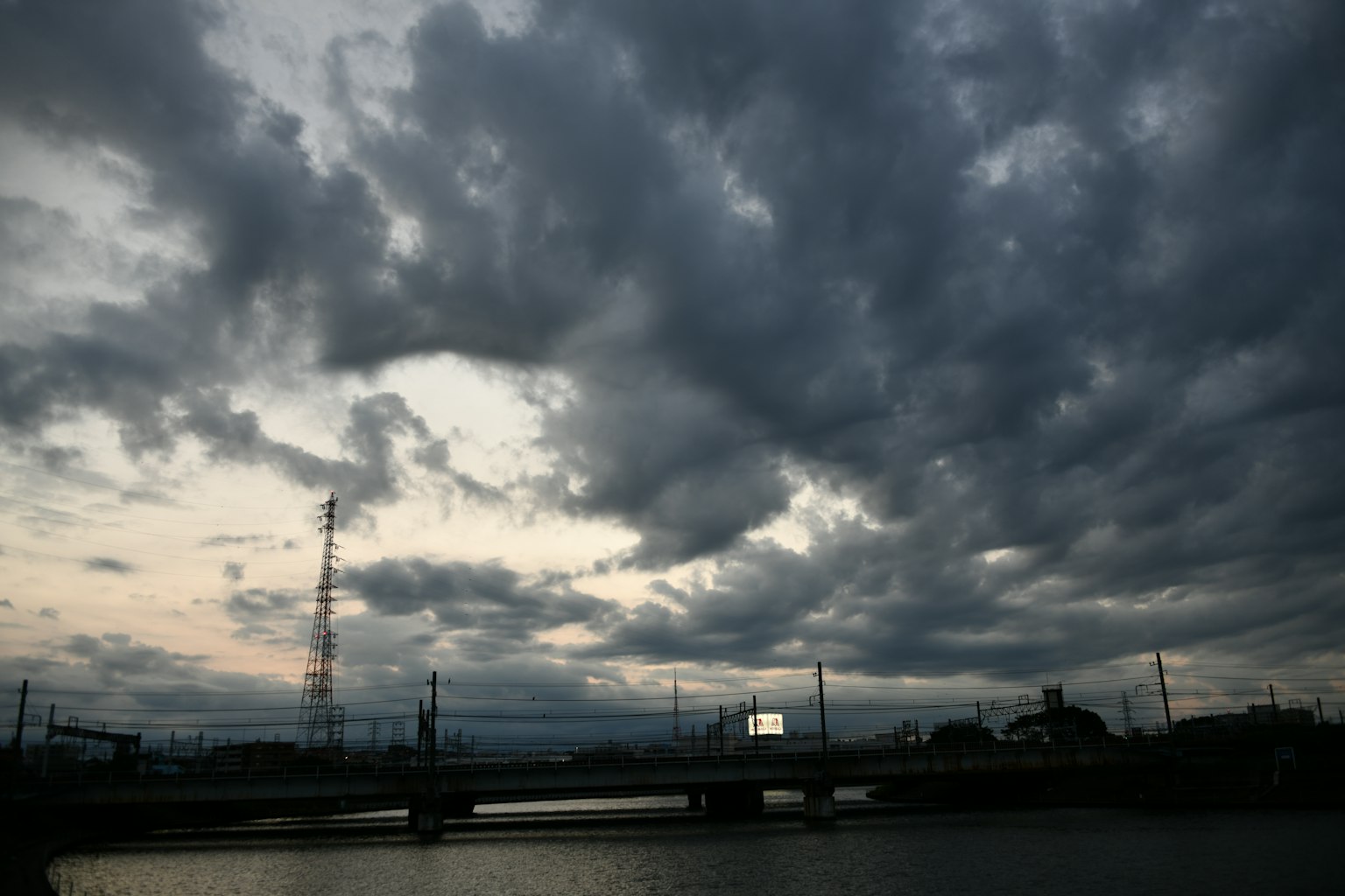 Cielo nuvoloso scuro sopra un fiume con silhouette di un ponte
