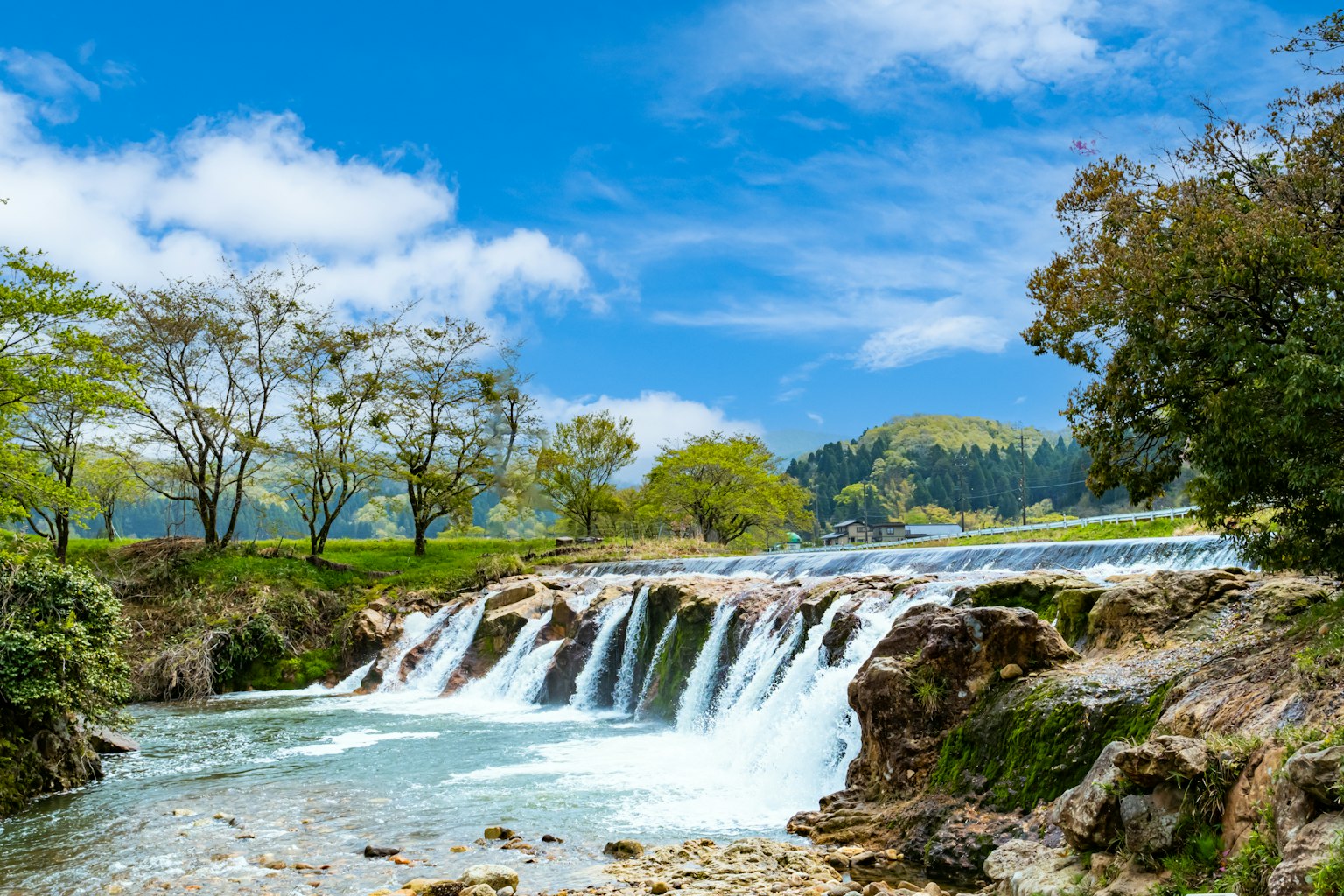 Ein kleiner Wasserfall umgeben von üppigem Grün unter einem blauen Himmel