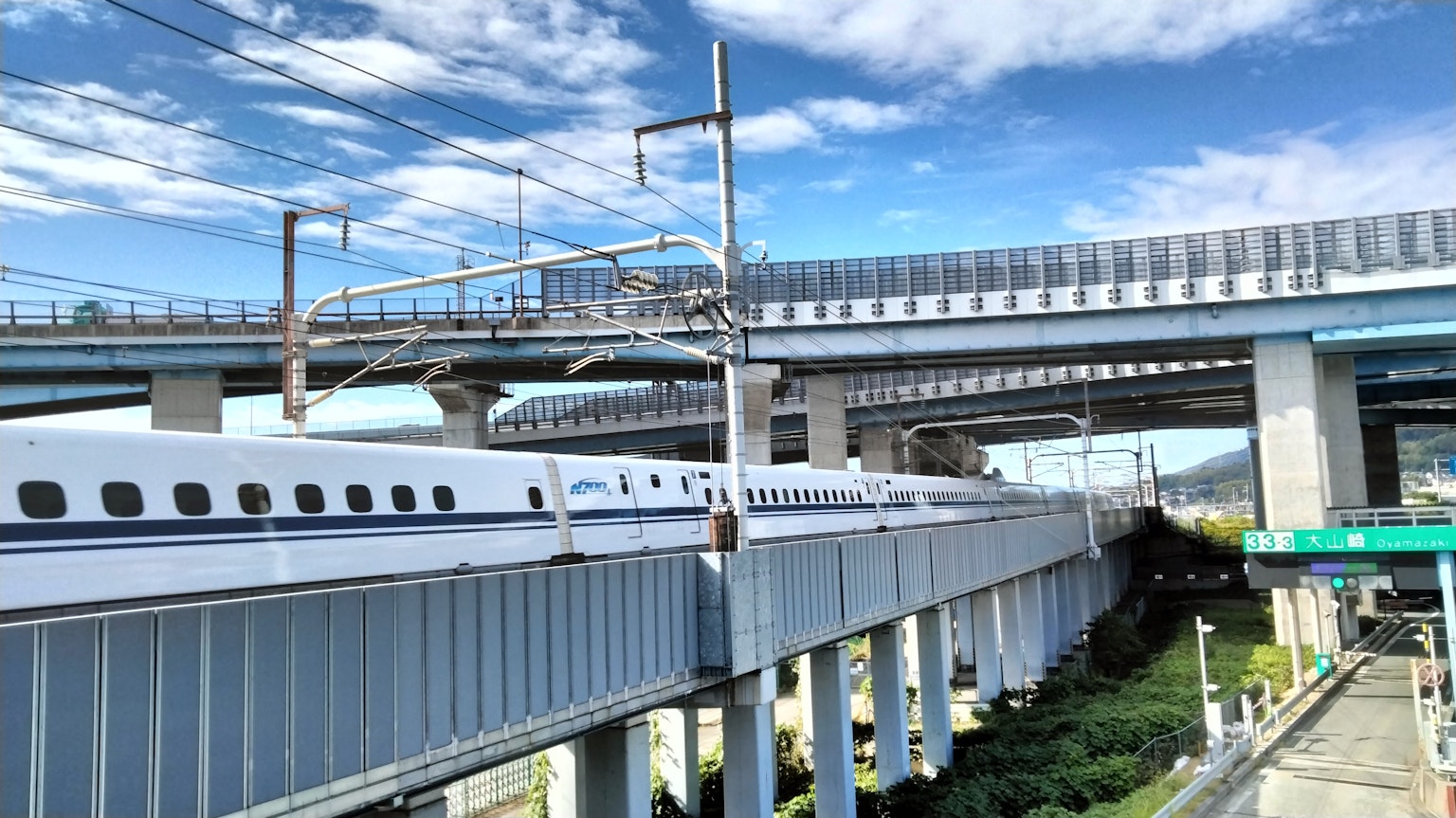 Tren Shinkansen pasando por debajo de una carretera con cielo azul