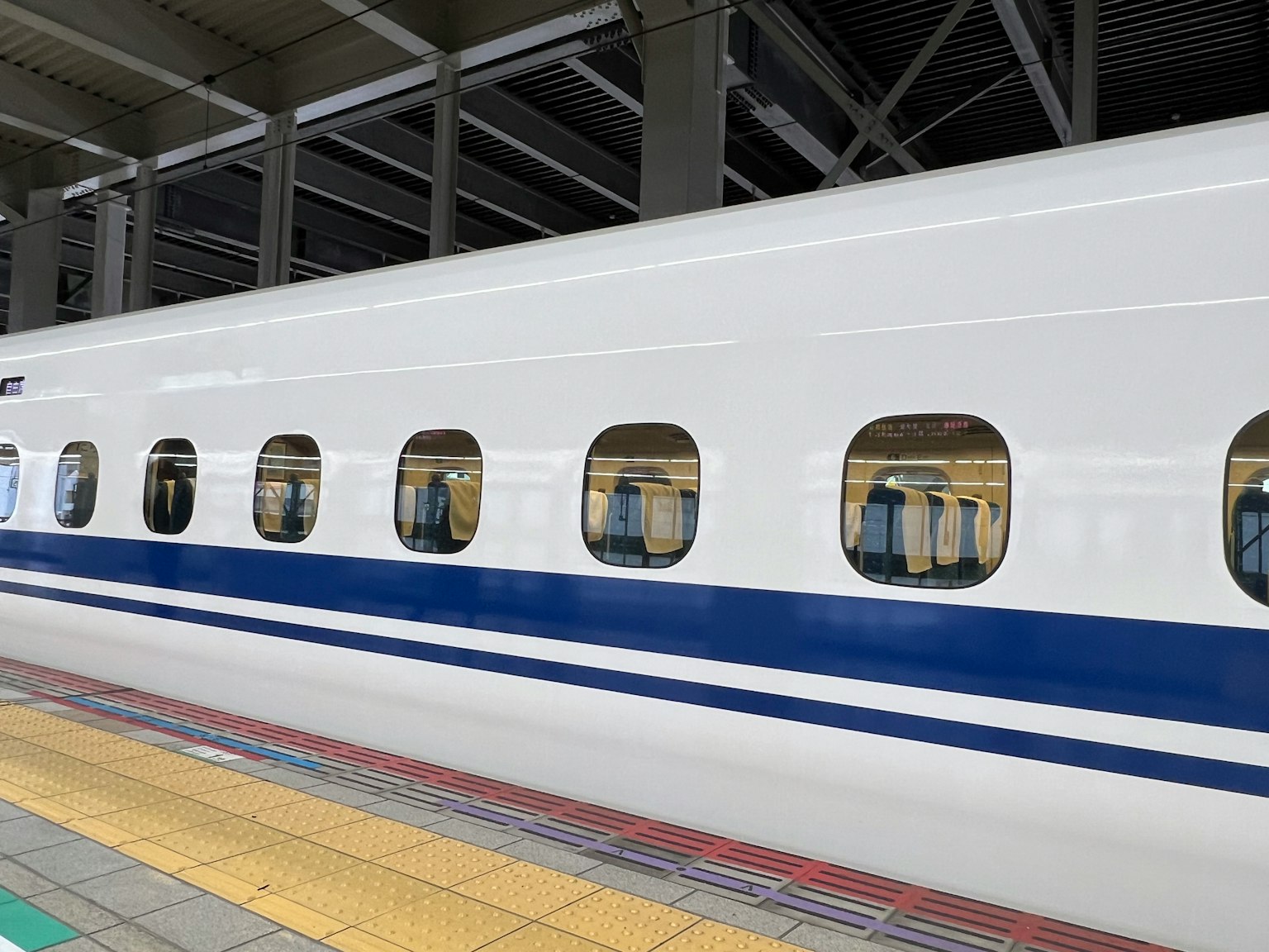 Góc nhìn bên hông của tàu Shinkansen với màu trắng và cửa sổ sọc xanh