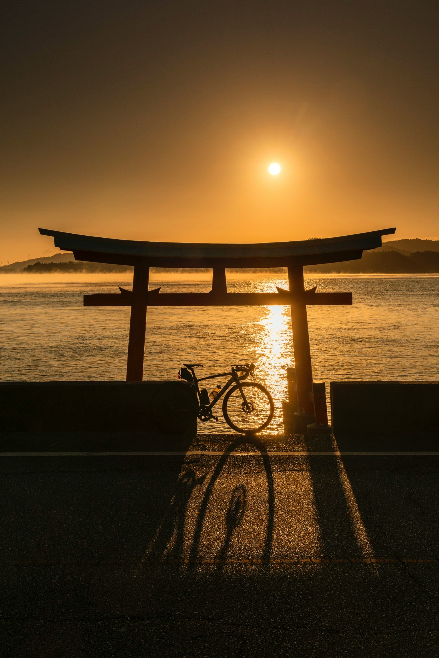 Porta torii in silhouette contro il tramonto con l'ombra di una bicicletta
