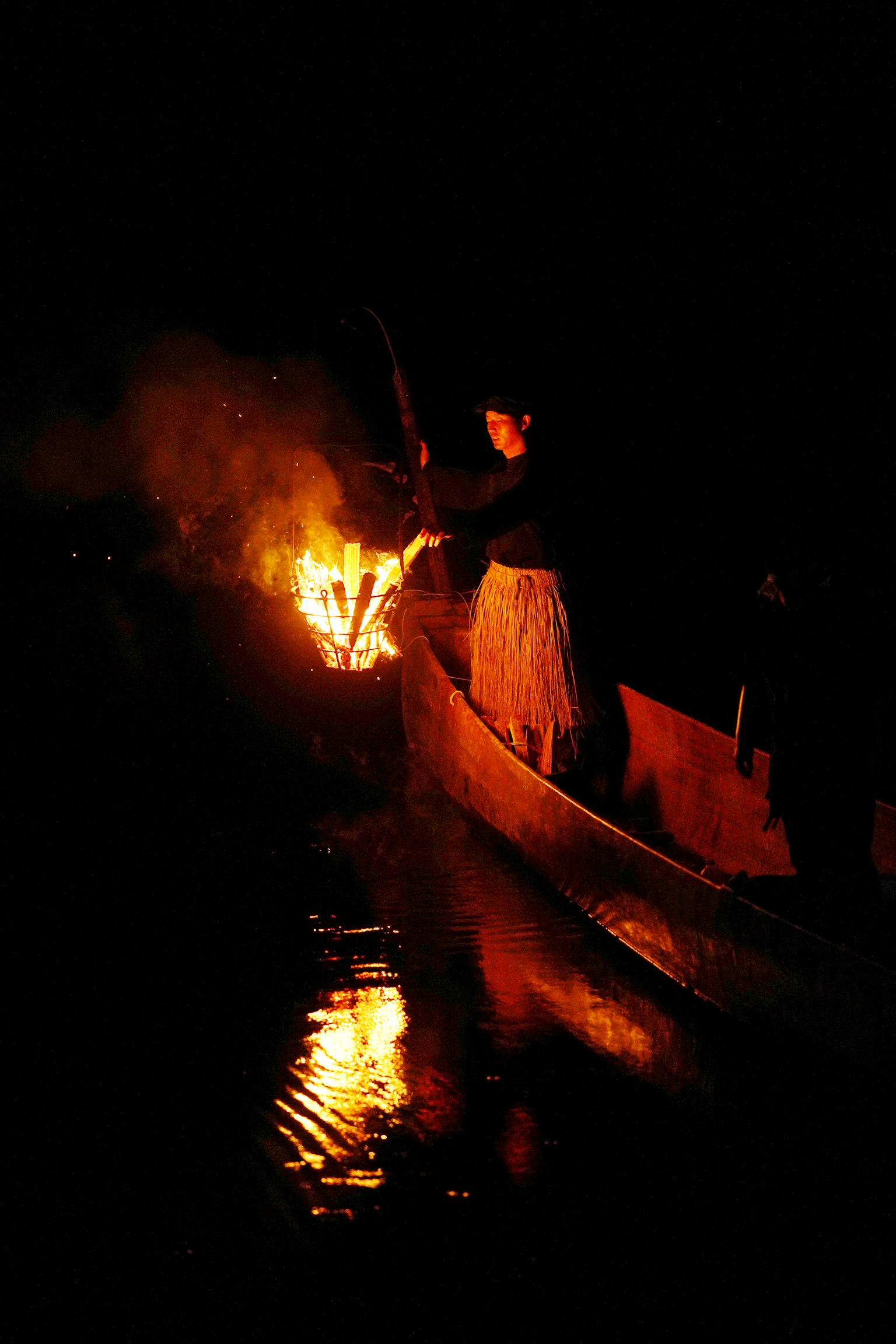 Person on a small boat holding fire reflecting on dark water