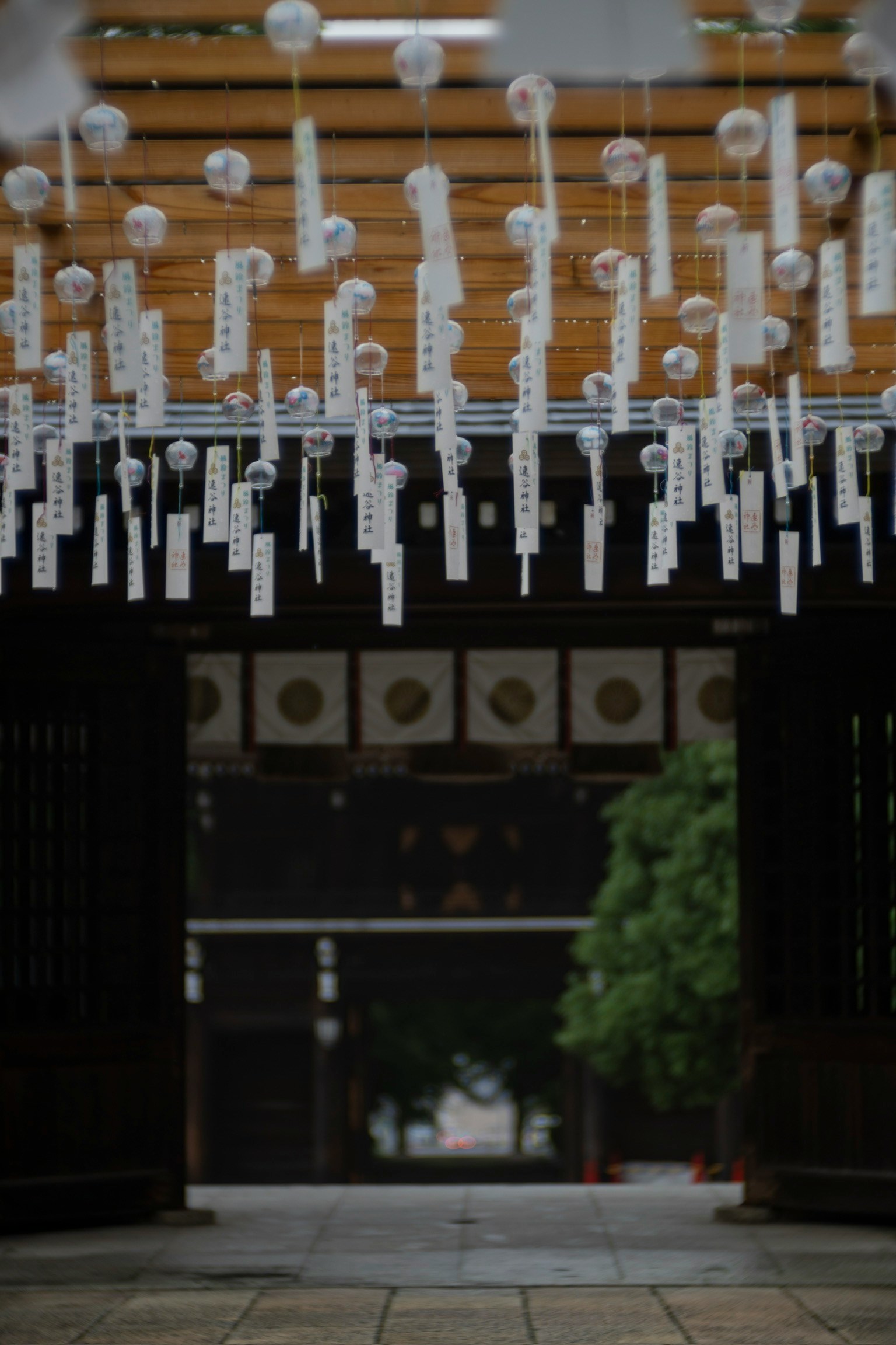 神社の入口に吊るされた白い短冊と風鈴が印象的な風景
