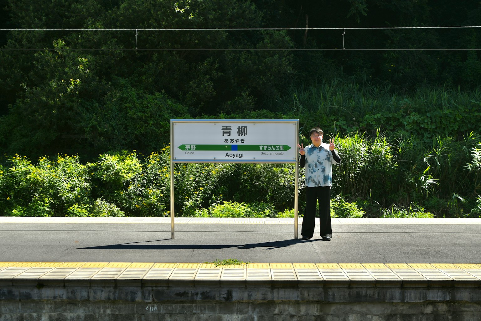 Person standing on a train platform next to a sign