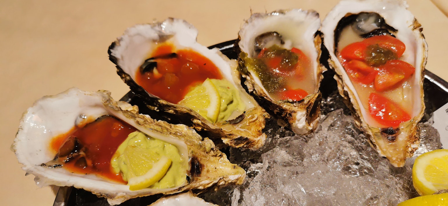 Ostras frescas dispuestas sobre hielo con salsa de tomate y rodajas de limón