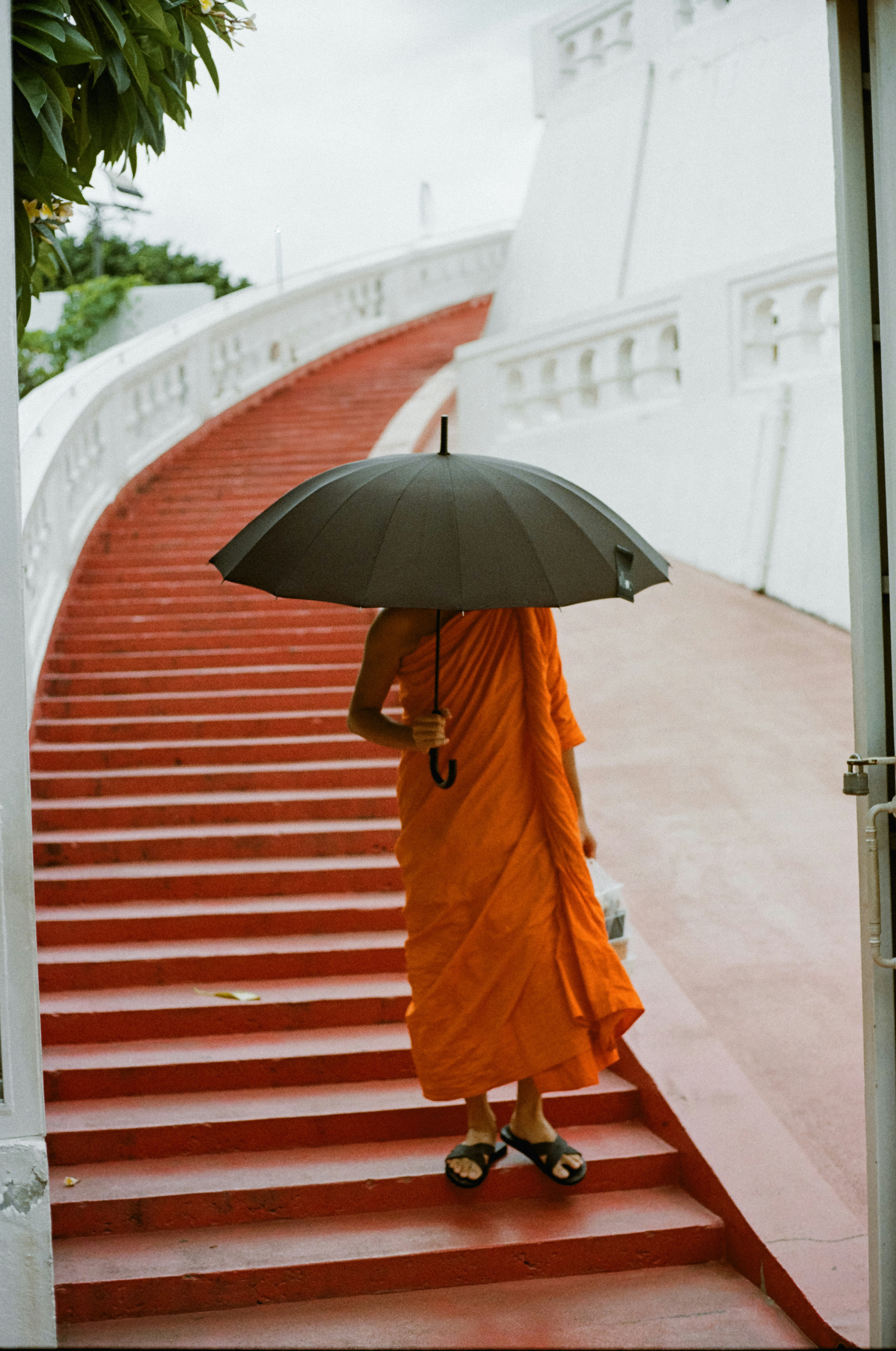 僧人手持雨傘從「Wat Saket Ratchawora Mahawihan」寺的階梯下行的景象