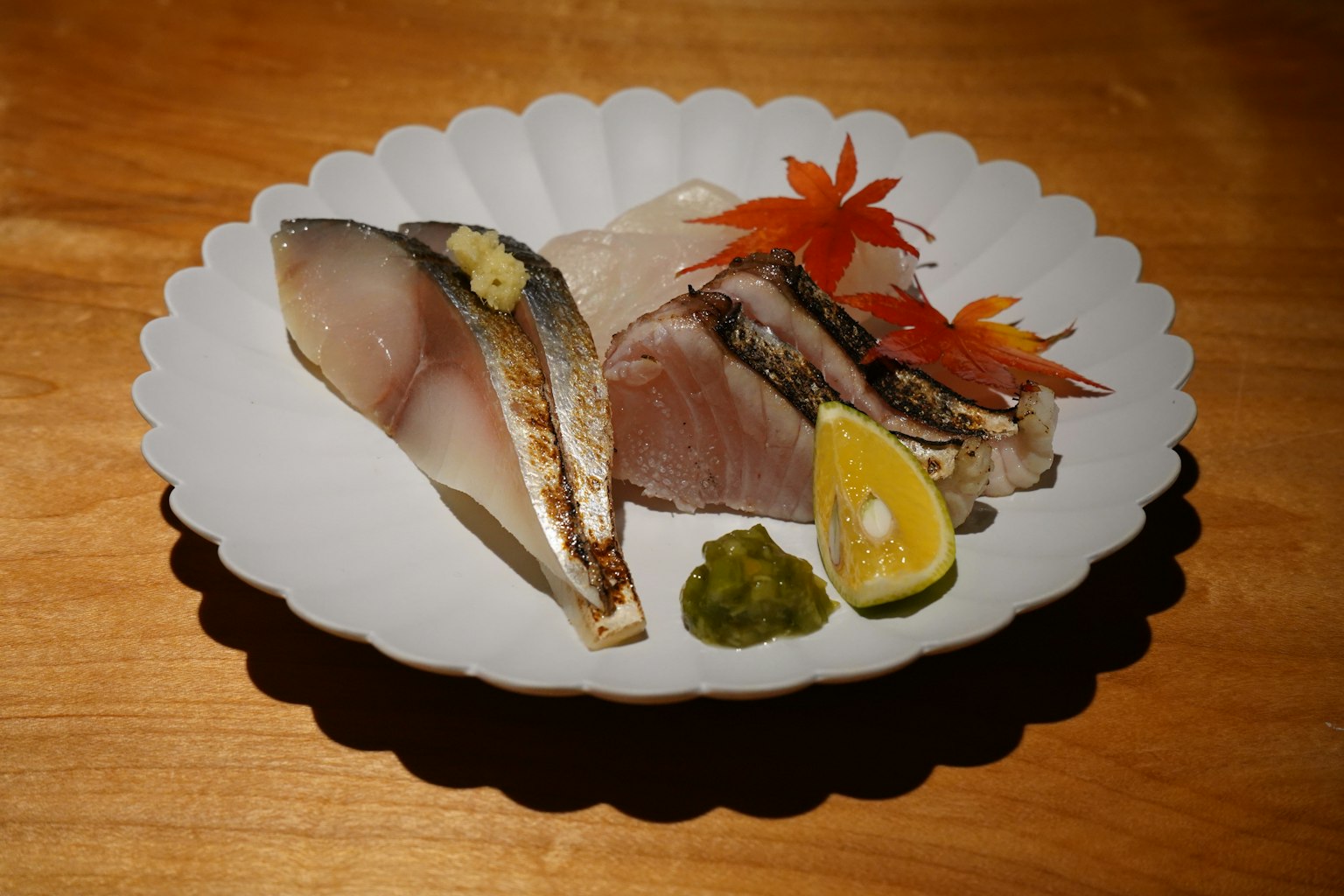 Sashimi tươi được sắp xếp trên đĩa trắng với lát chanh wasabi và lá phong
