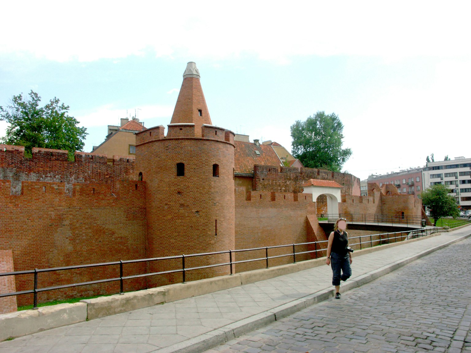 Una donna che cammina lungo muri di castello in mattoni rossi e una torre