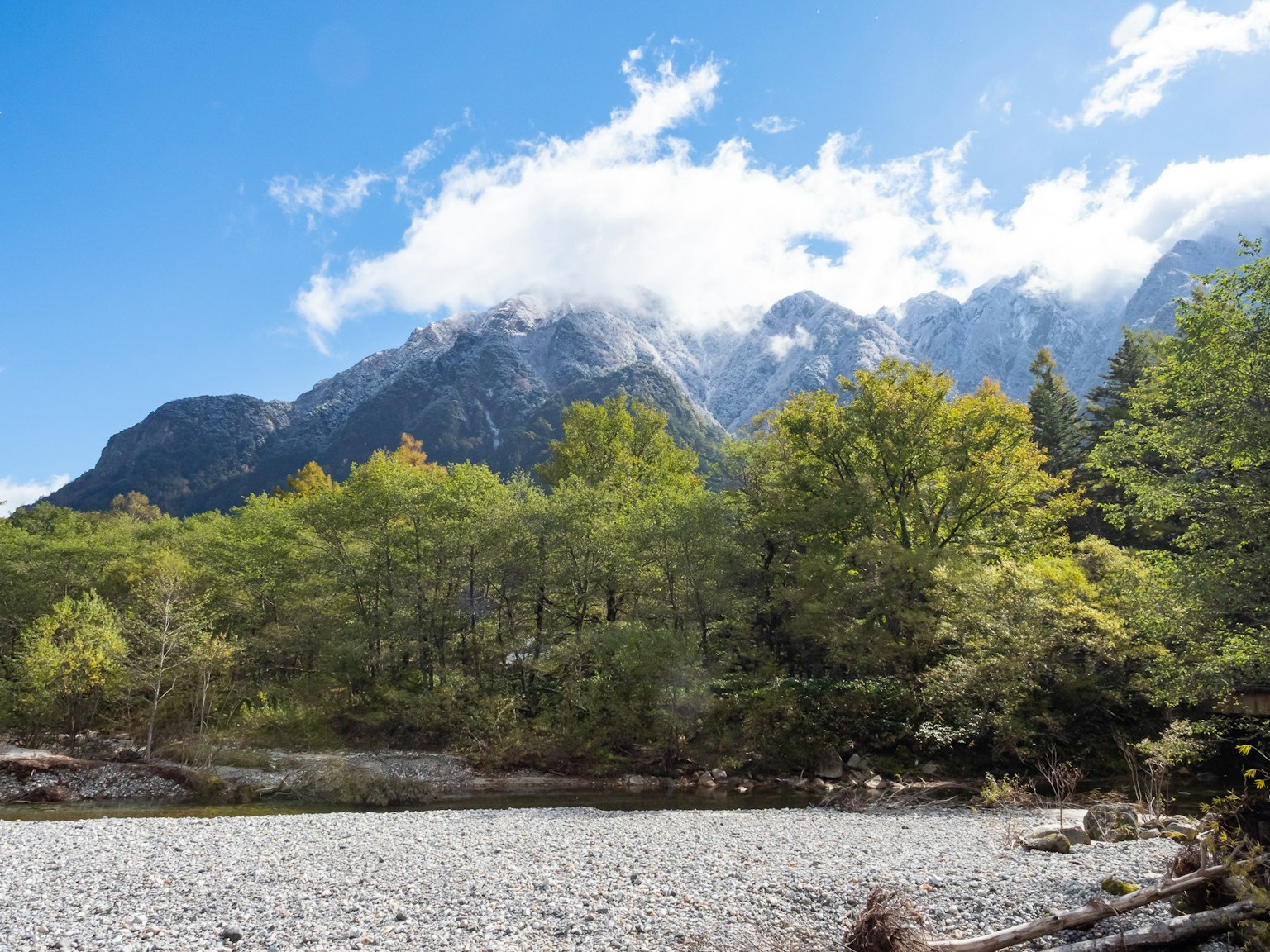Malersicher Blick auf Berge mit Wolken und grünen Bäumen unter einem blauen Himmel