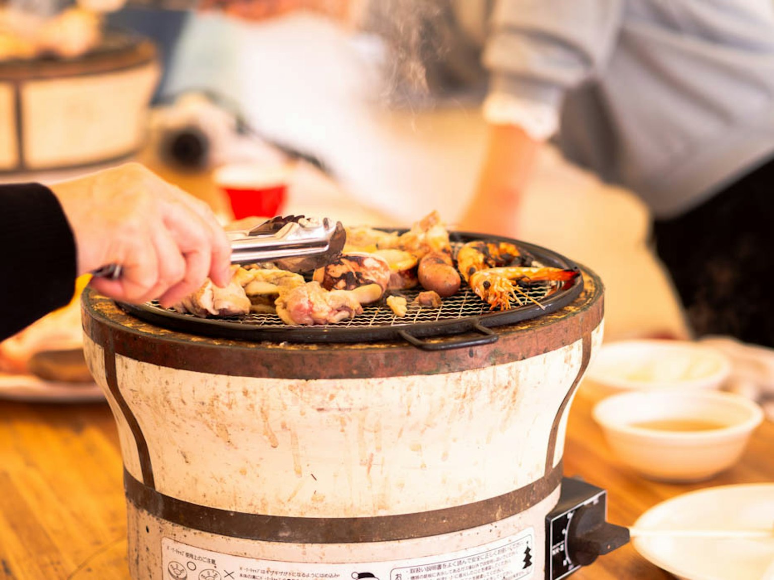 Hands cooking on a grill with various meats and vegetables