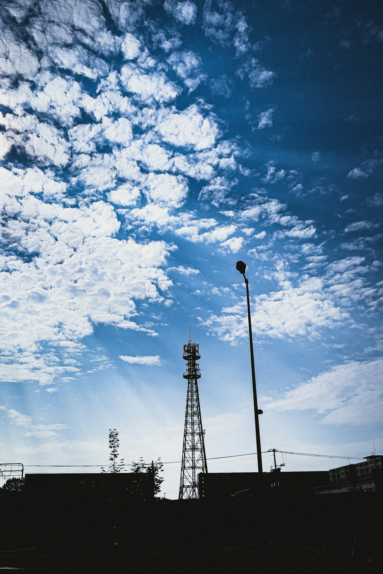 Silueta de una torre de comunicación contra un cielo azul con nubes blancas