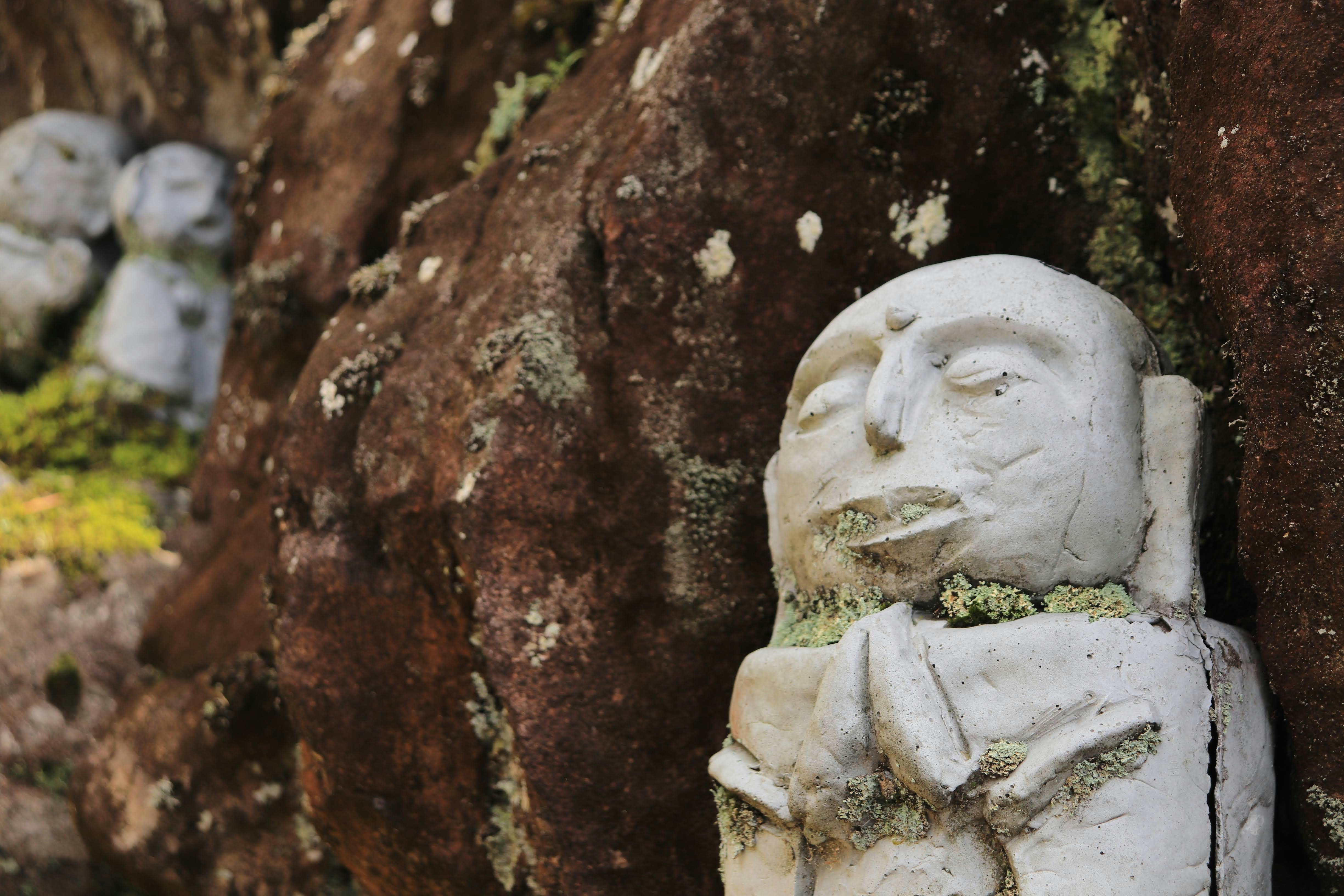 mossy stone Jizo statue beside an old stone wall in a temple corner