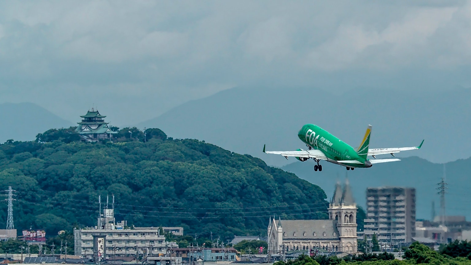 Green airplane taking off against a cloudy sky with a cityscape in the background
