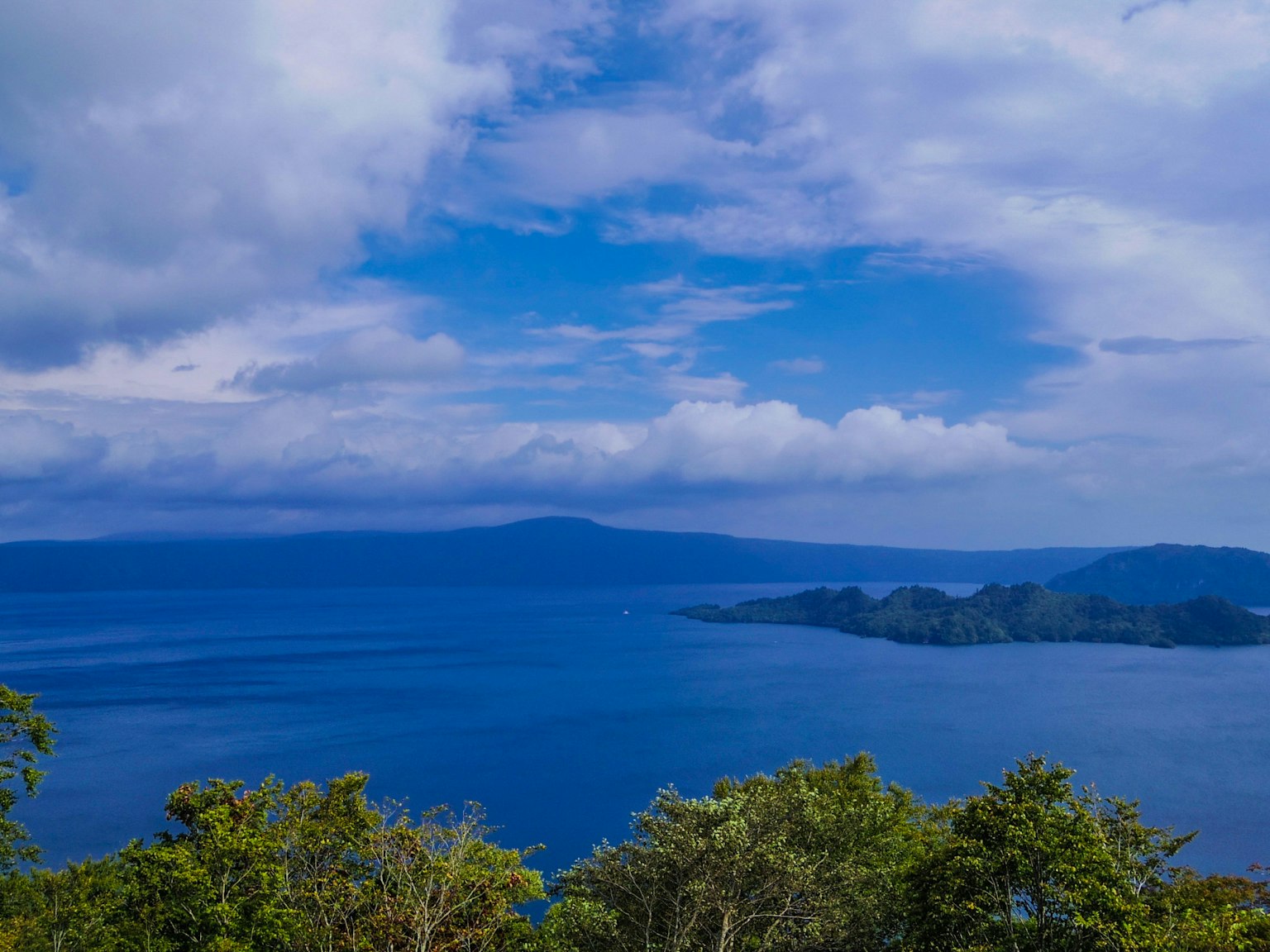ทิวทัศน์ของทะเลสาบสีน้ำเงินที่ล้อมรอบด้วยพืชพรรณเขียวขจี