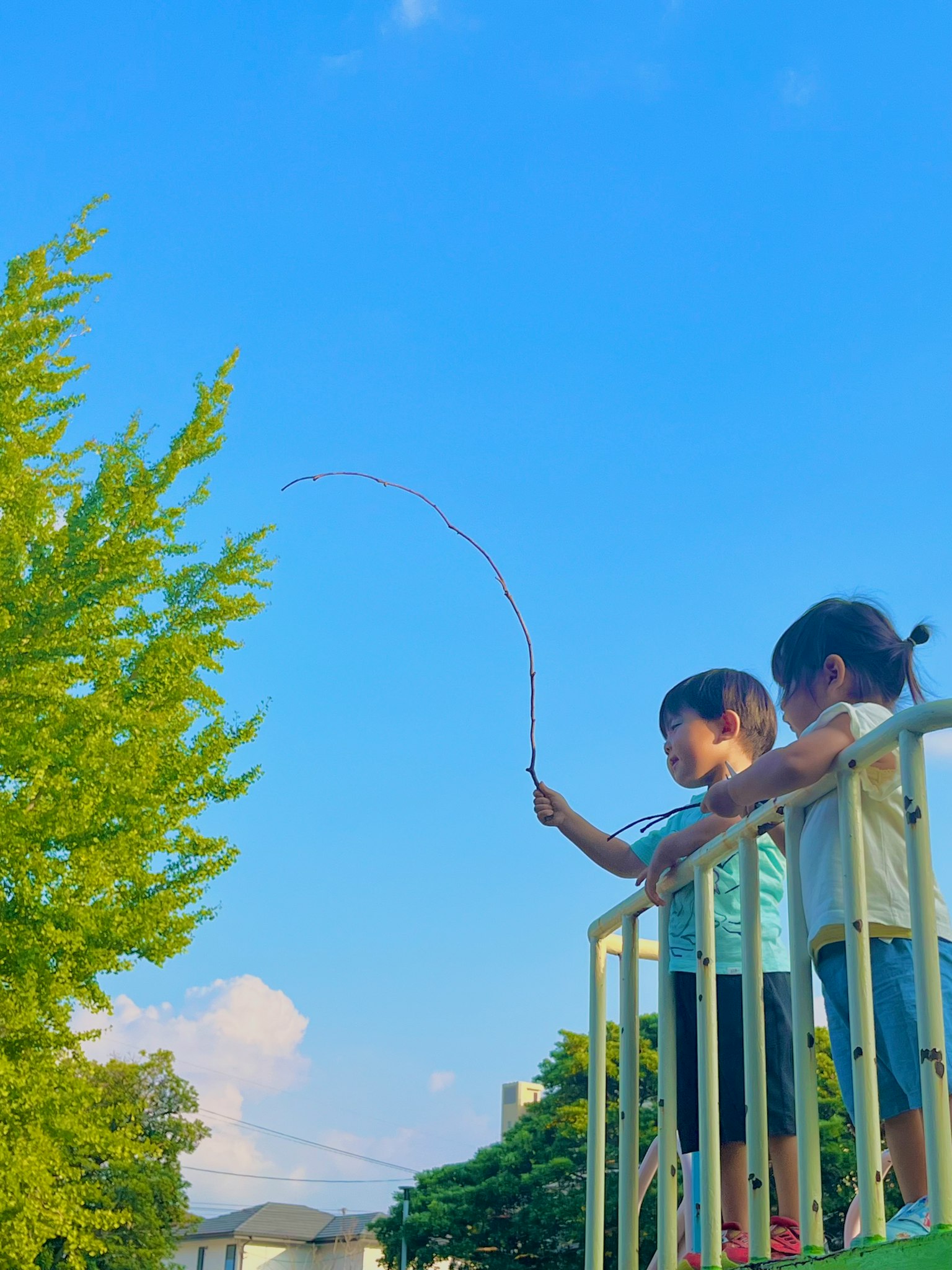 青空の下で遊ぶ二人の子供たちが木の枝を持っている