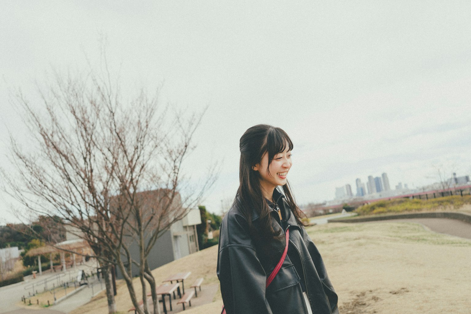 Eine lächelnde Frau in einem Park mit einer Stadtsilhouette im Hintergrund