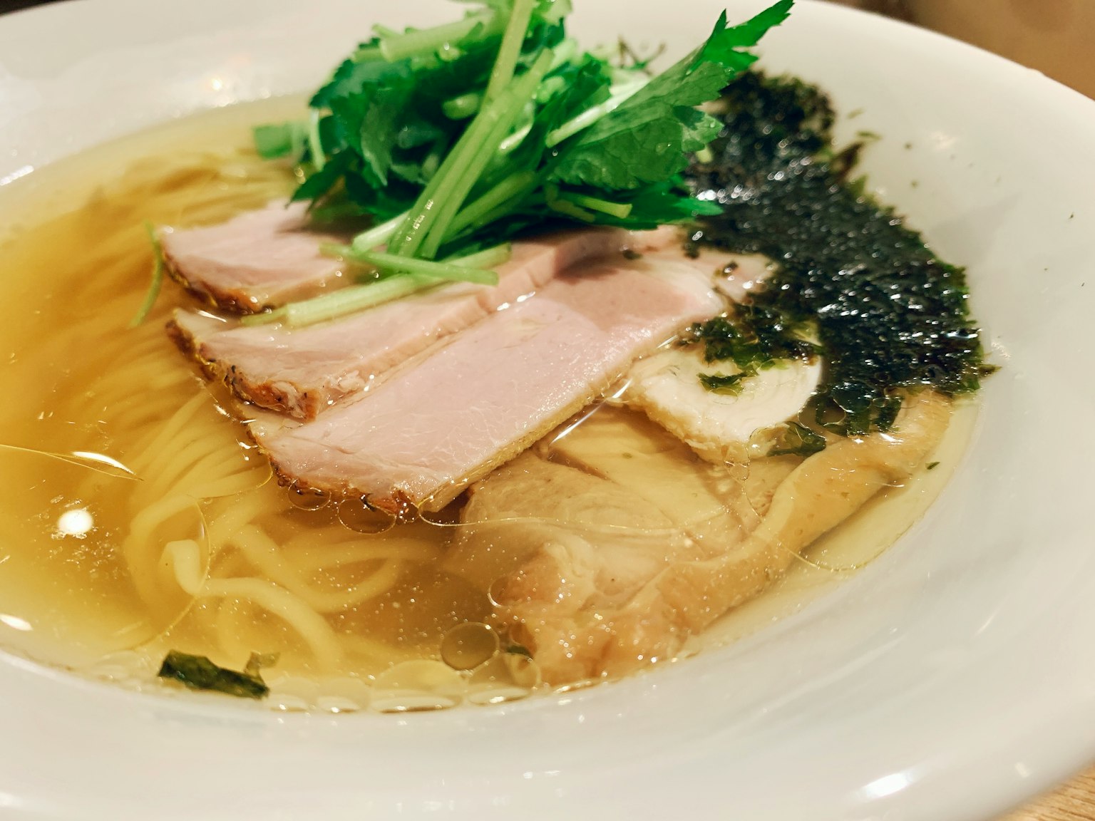 Mangkuk ramen dengan irisan char siu dan herba hijau dalam kaldu bening