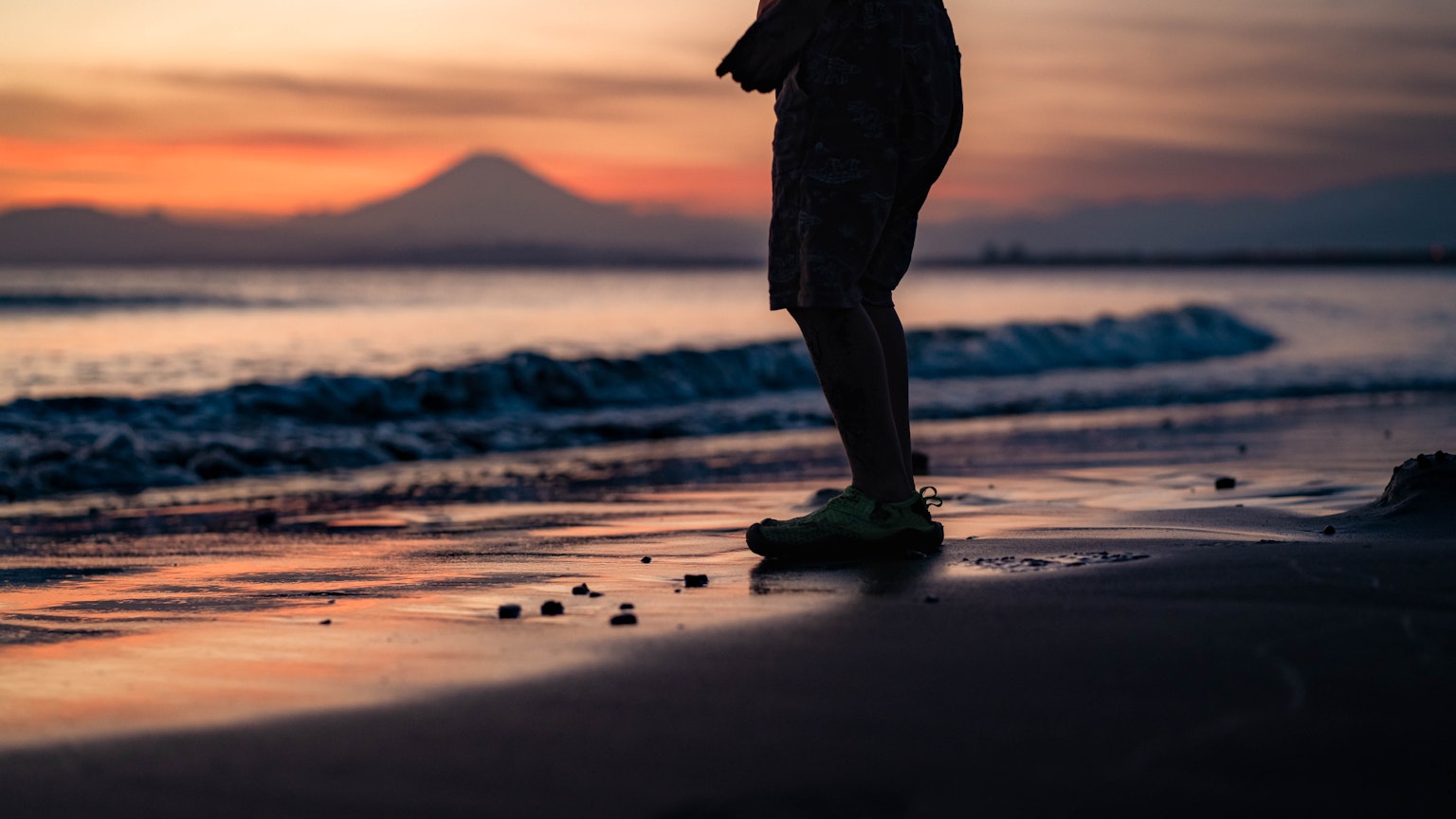 Silhouette einer Person, die am Strand während des Sonnenuntergangs mit Wellen steht