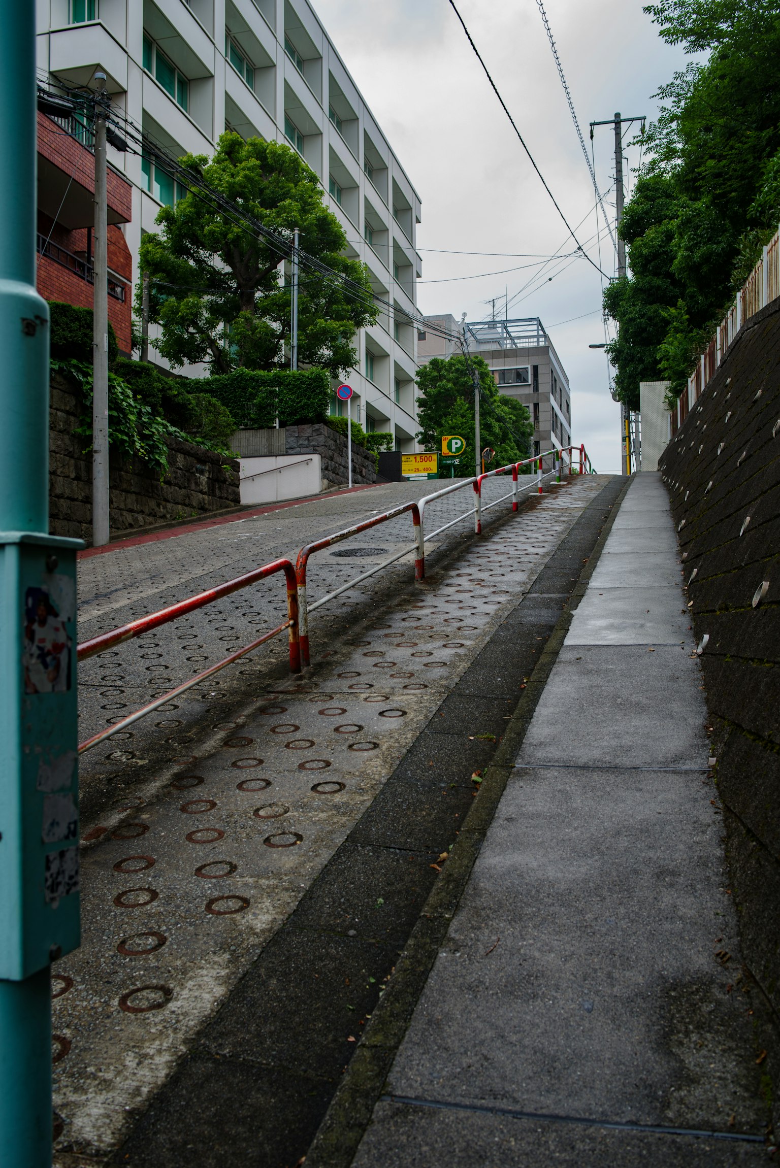 Calle inclinada con una barandilla roja y vegetación circundante