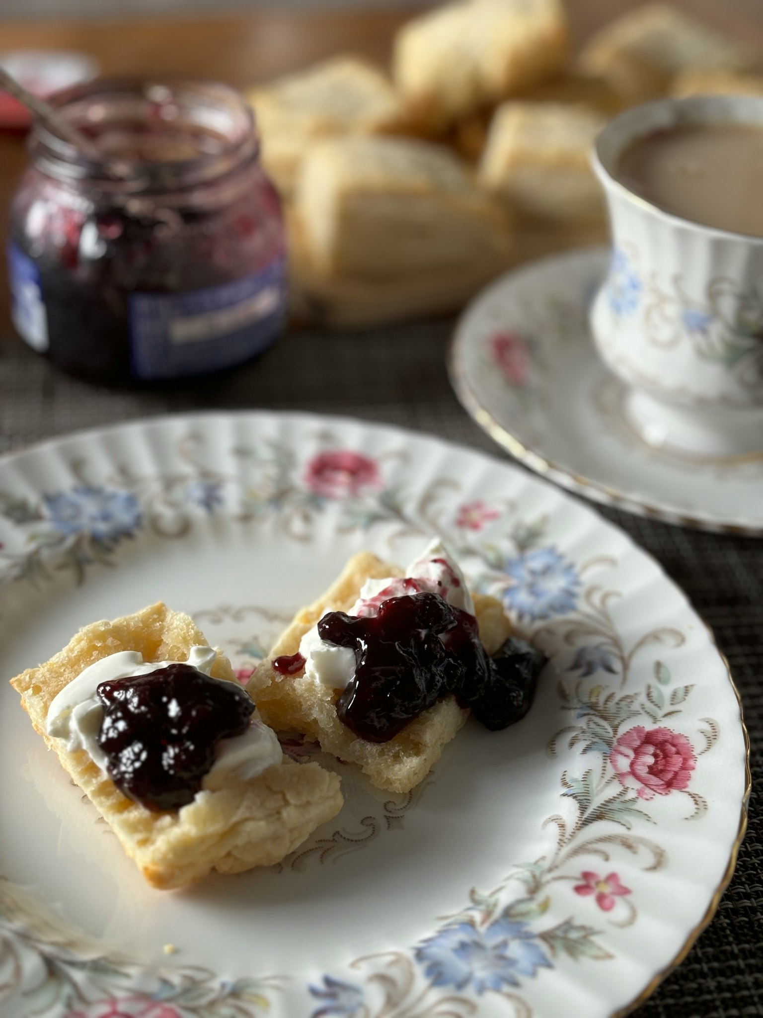 Plato de scones cubiertos con crema y mermelada junto a una taza de té