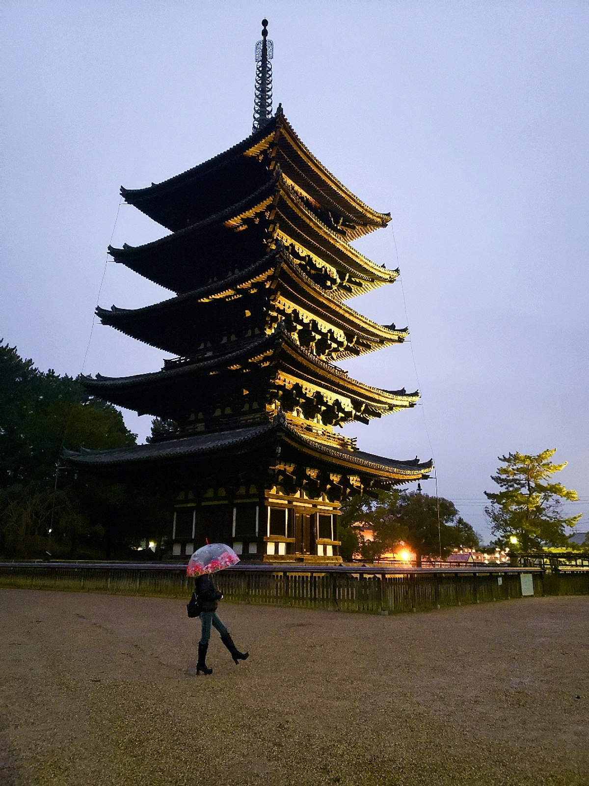 夕暮れの五重塔と広場を歩く傘の人