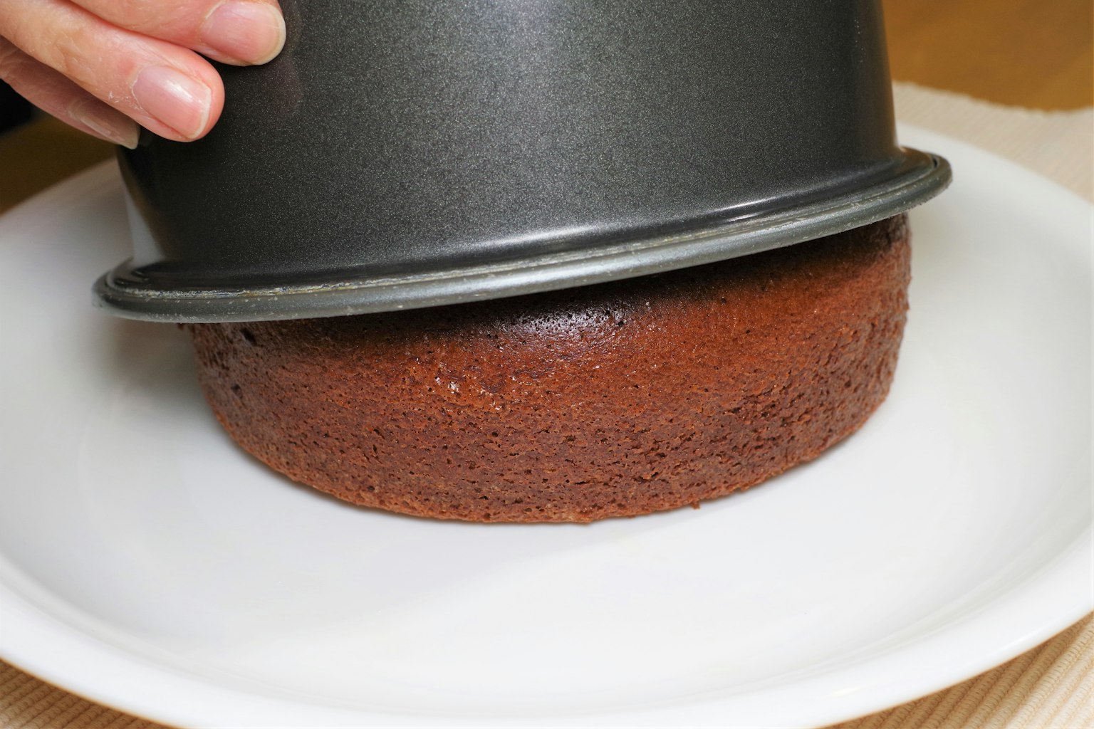 Main tenant un moule à gâteau au-dessus d'un gâteau au chocolat sur une assiette blanche