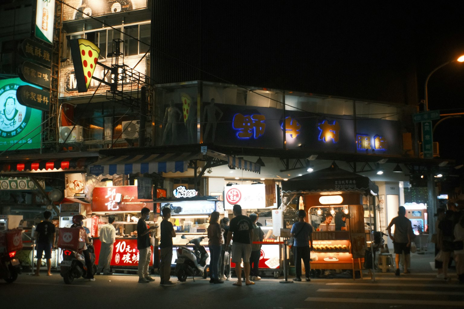 ตลาดกลางคืนที่คึกคักพร้อมป้ายไฟสว่างและแผงขายอาหาร