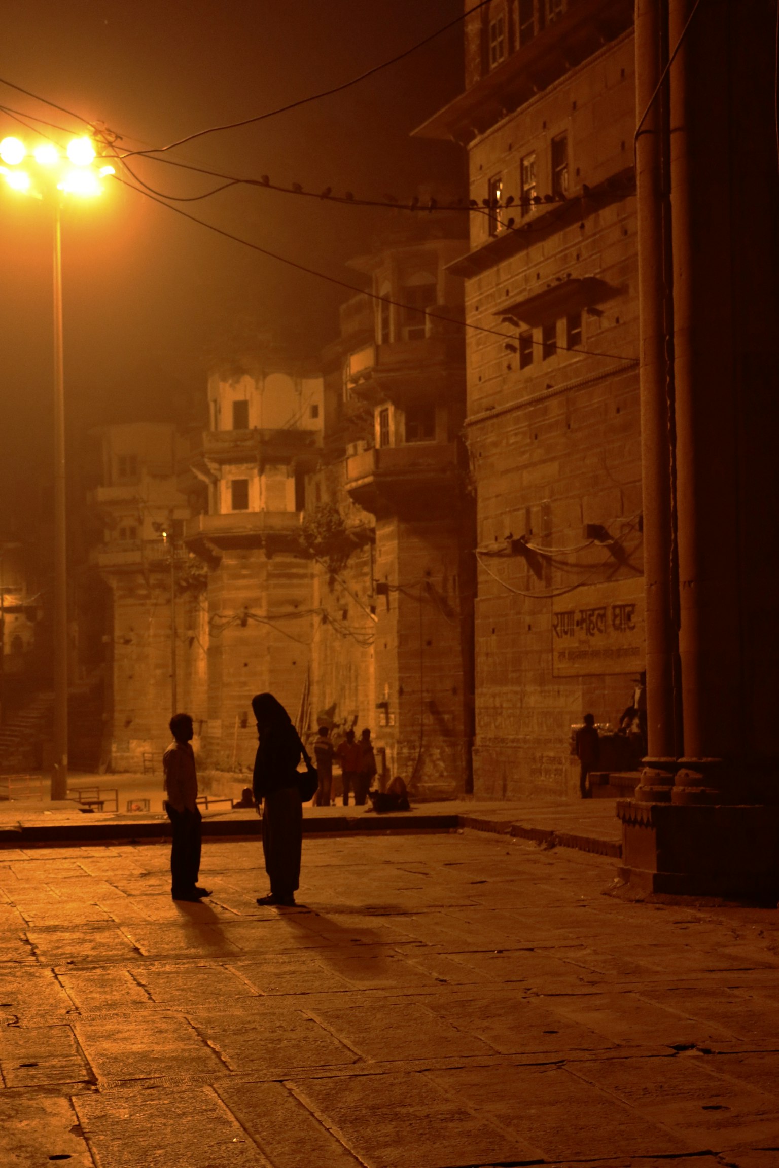 Siluetas de personas junto a edificios antiguos a lo largo del río Ganges por la noche