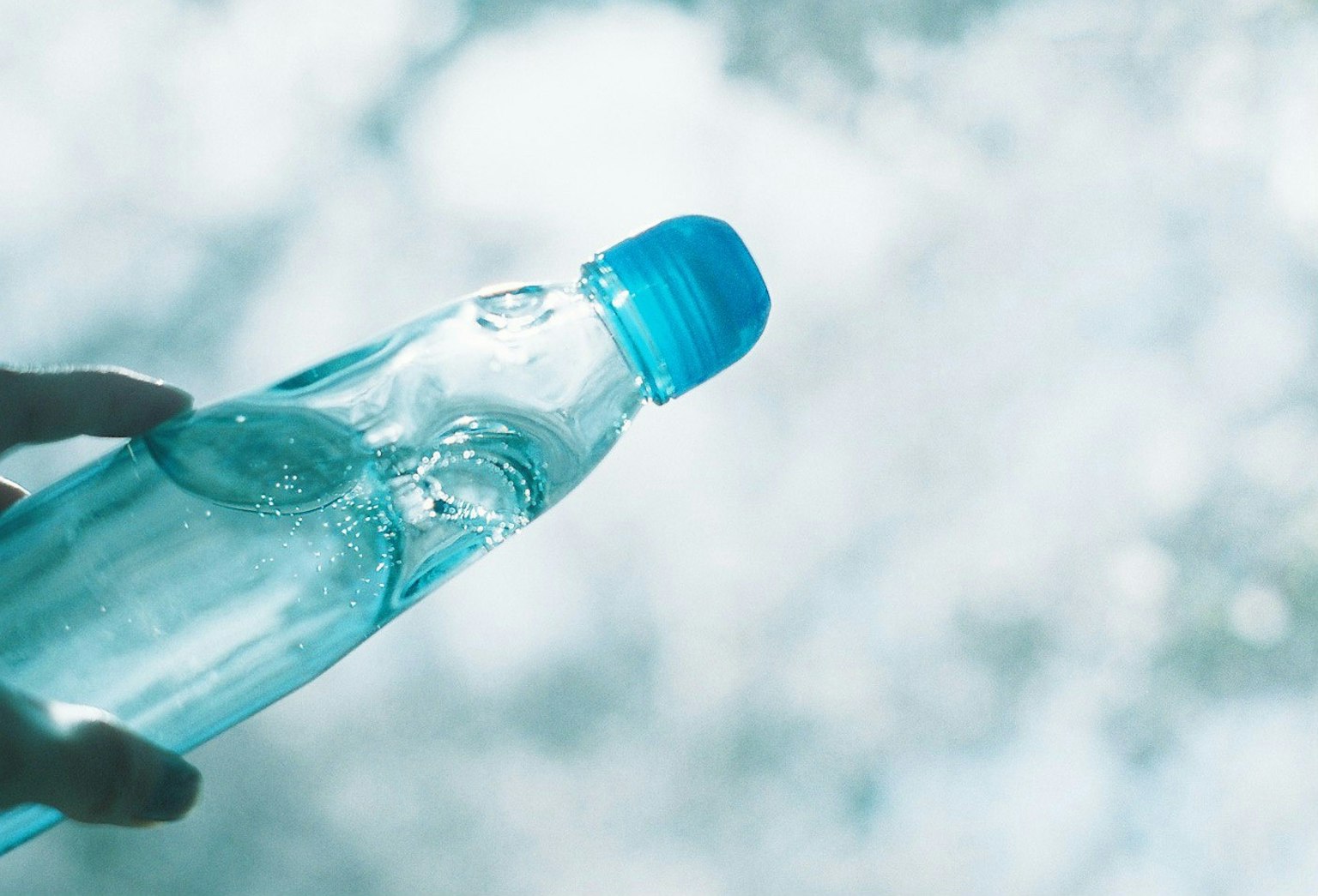 A clear water bottle held in hand with droplets on it